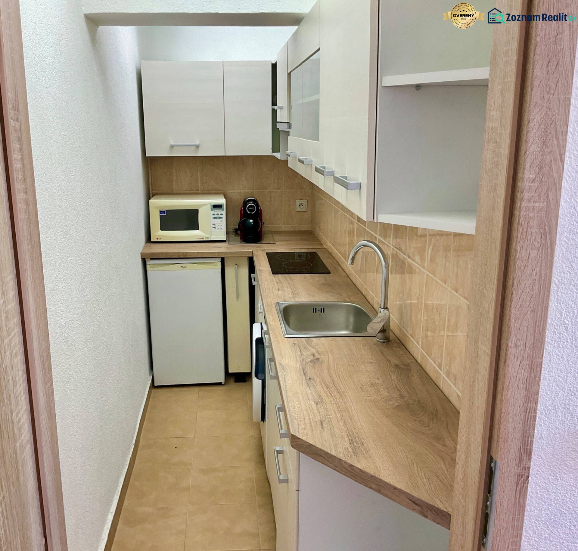 Küche in einer Einzimmerwohnung mit Holzdekor, Mikrowelle und eingebauten Geräten.