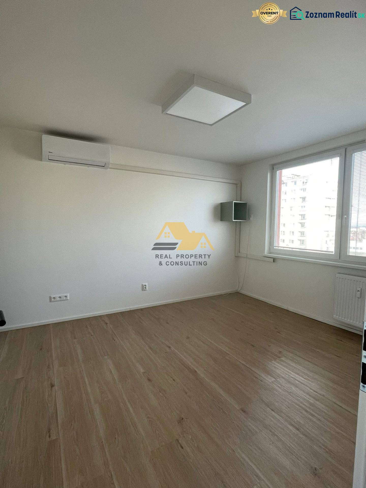 Ein Zimmer mit weißen Wänden und einem Boden in Holzoptik in einer Einzimmerwohnung.