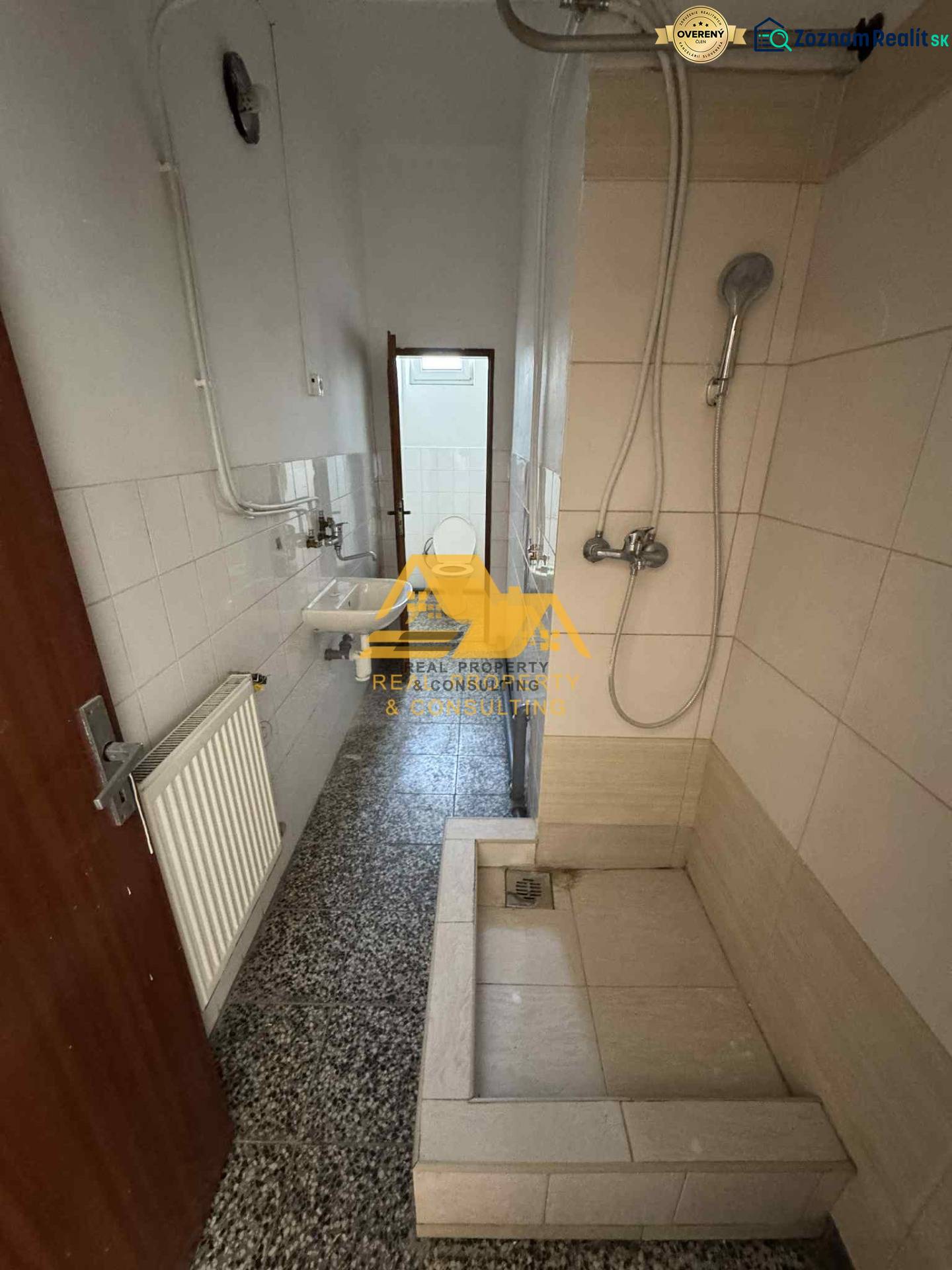 Badezimmer in einem Studio-Apartment mit einer einfachen Duschkabine, einem Waschbecken und Fliesen.