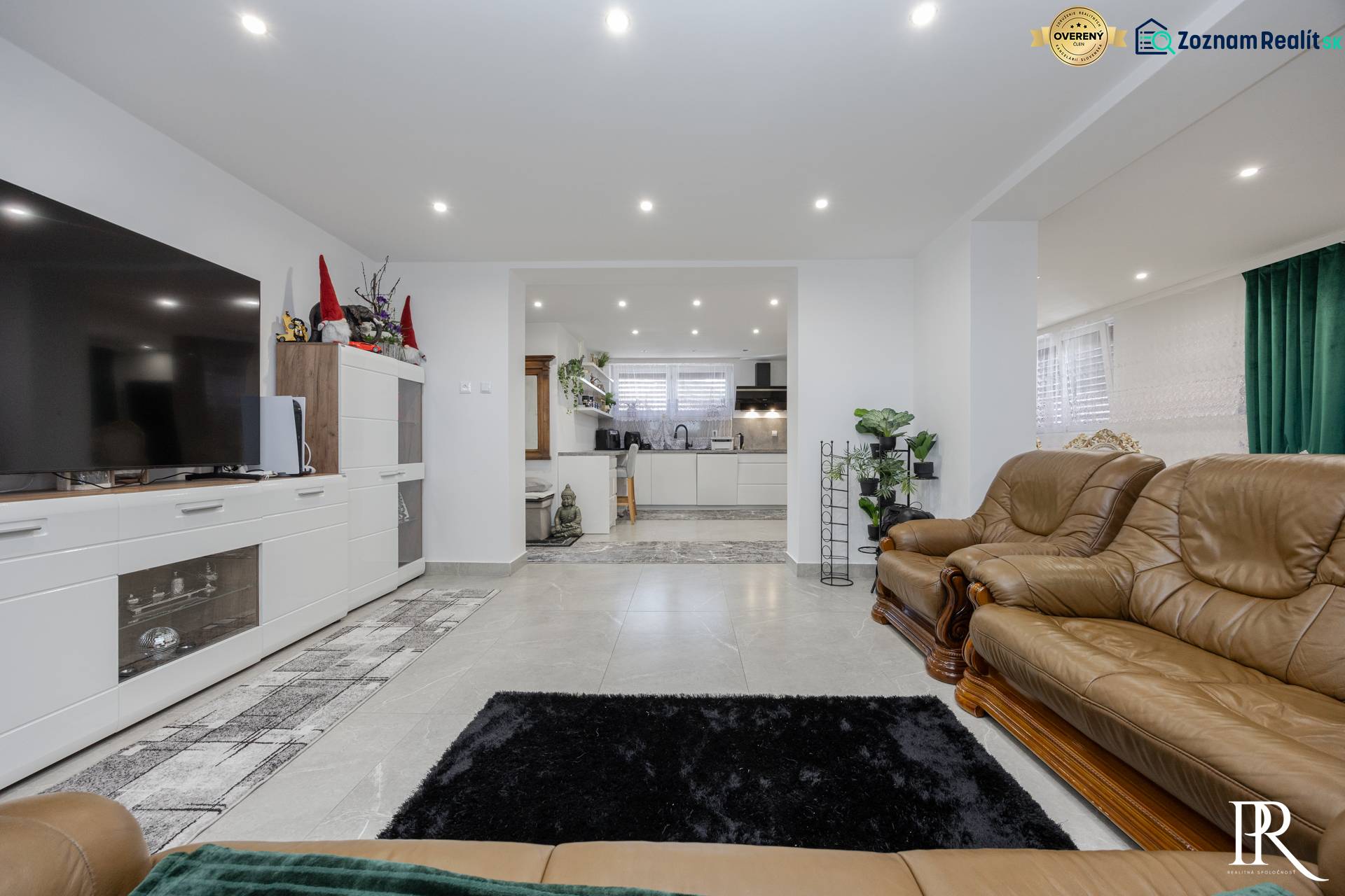 Wohnzimmer mit Ledermöbeln, Fliesenboden und Küchenzeile in einem Einfamilienhaus.