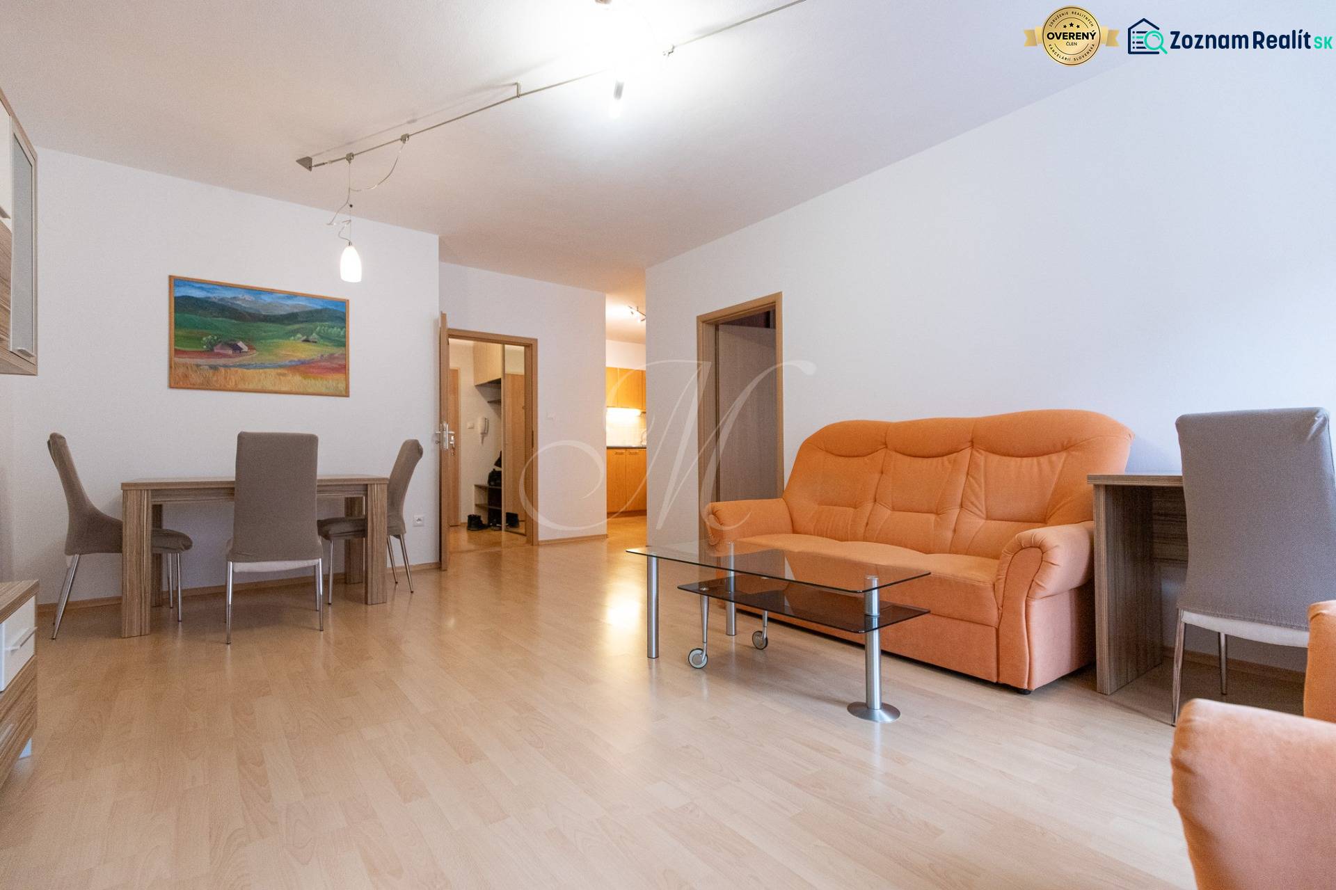 Wohnzimmer einer Zweizimmerwohnung mit einem orangefarbenen Sofa und einem Boden in Holzoptik.