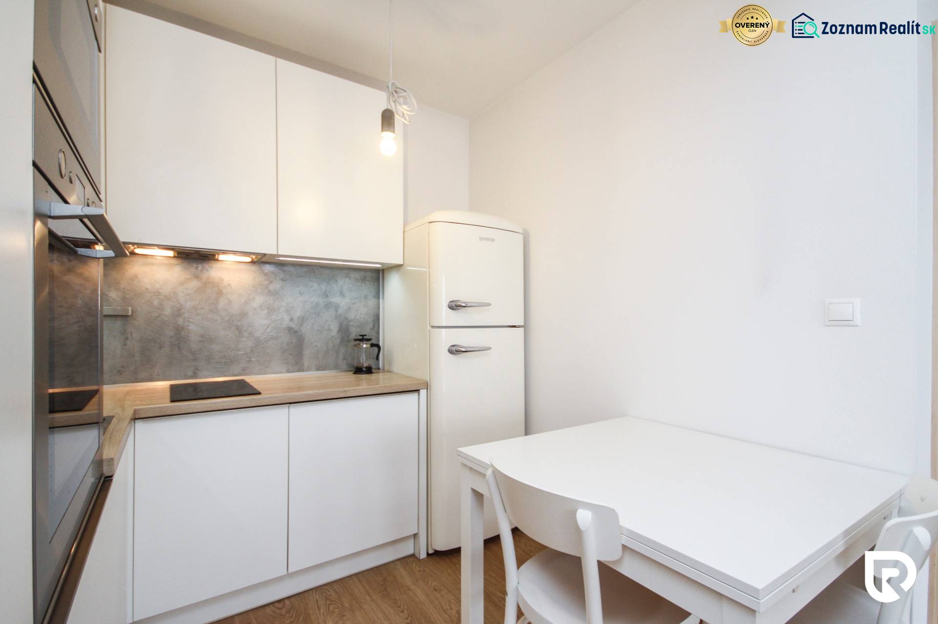 Küche in einer 2-Zimmer-Wohnung mit weißer Einrichtung und Boden in Holzoptik.