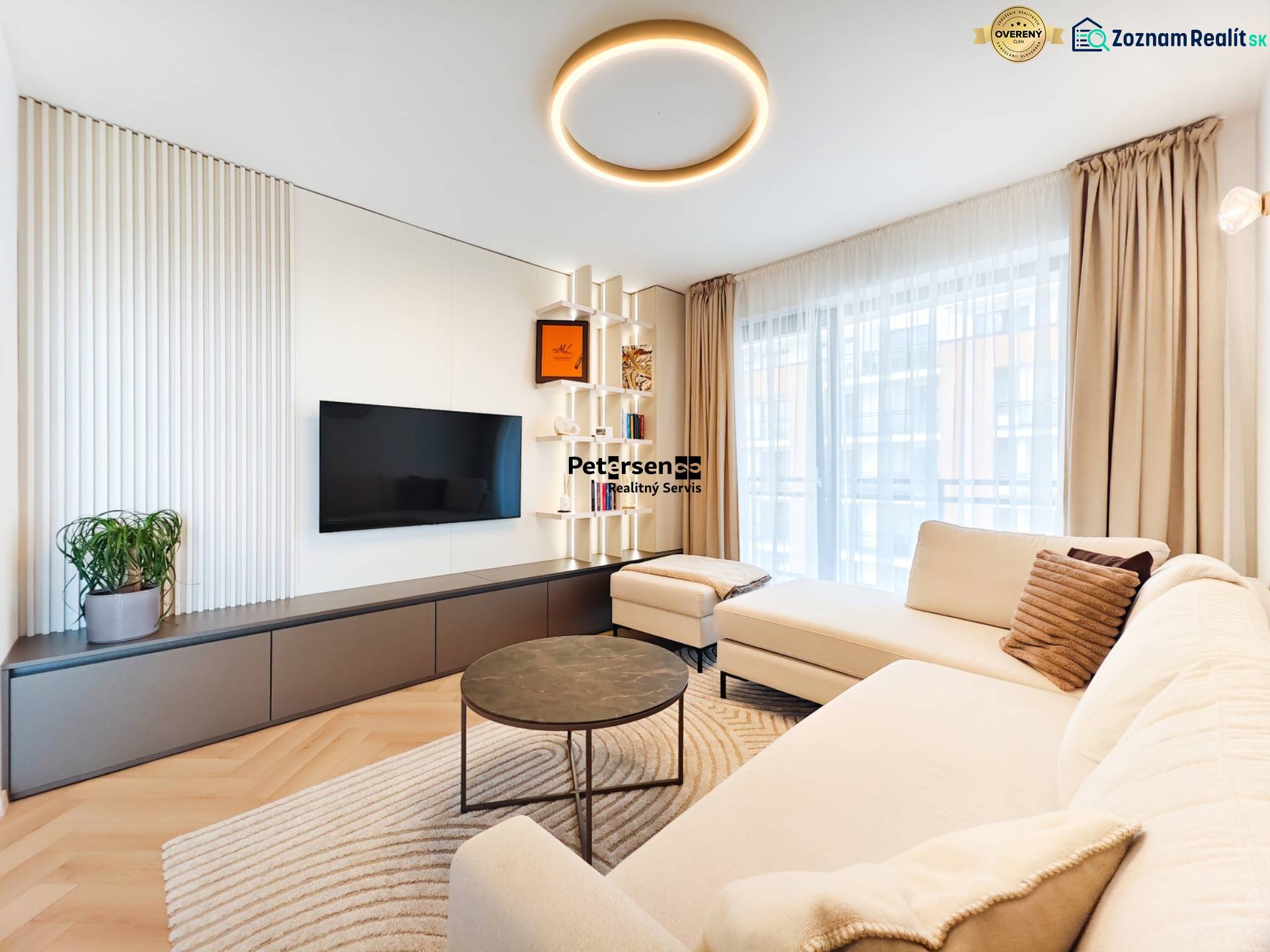 Wohnzimmer in einer Zweizimmerwohnung mit Sofa, Fernseher und Boden in Holzoptik.