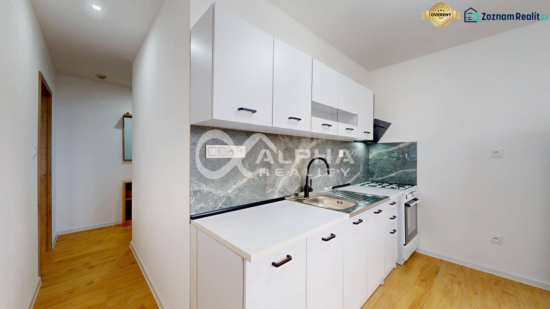 Küche in einer Einzimmerwohnung mit weißen Schränken und einem Boden in Holzoptik.