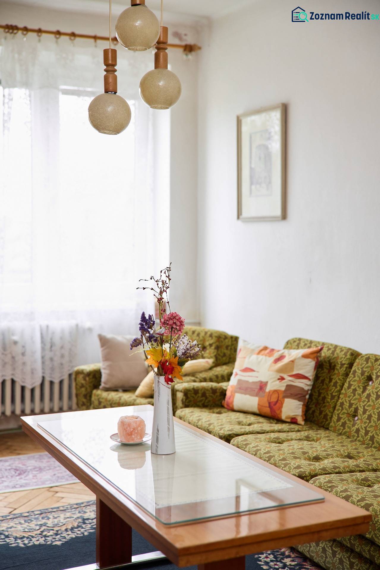 Helles Wohnzimmer in einer 3-Zimmer-Wohnung mit Sofa, Tisch und dekorativen Blumen in einer Vase.