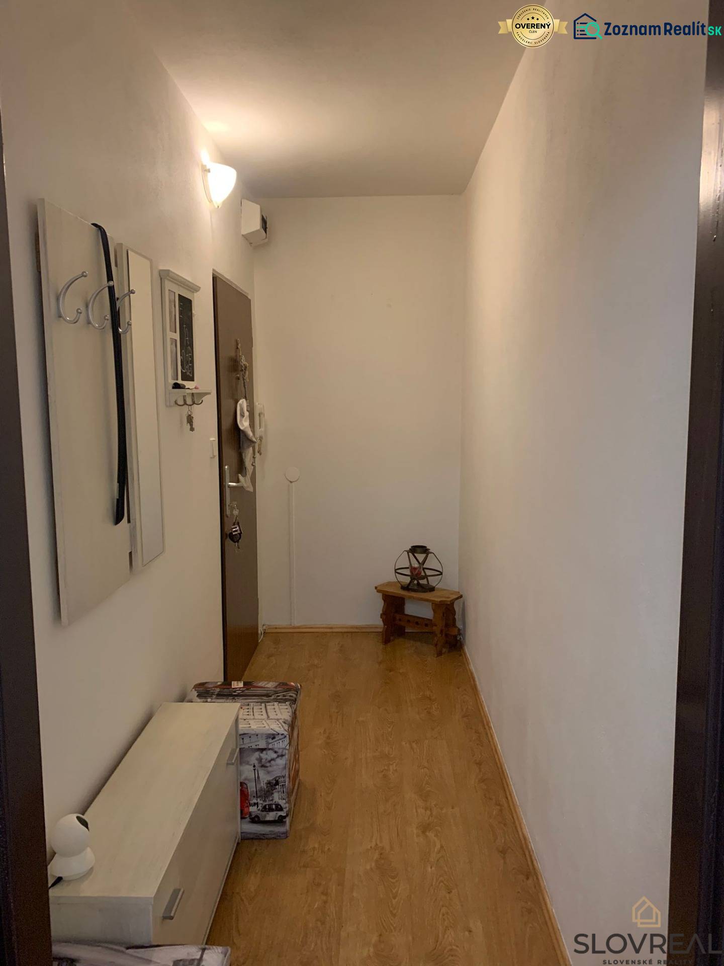 Ein schmaler Flur mit weißen Wänden, einem Boden in Holzoptik und minimalistischen Möbeln.