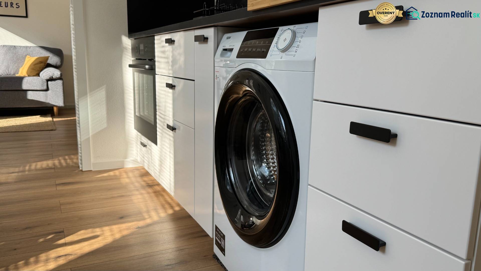 Küche in einer Einzimmerwohnung mit eingebauter Waschmaschine und Boden mit Holzdekor.