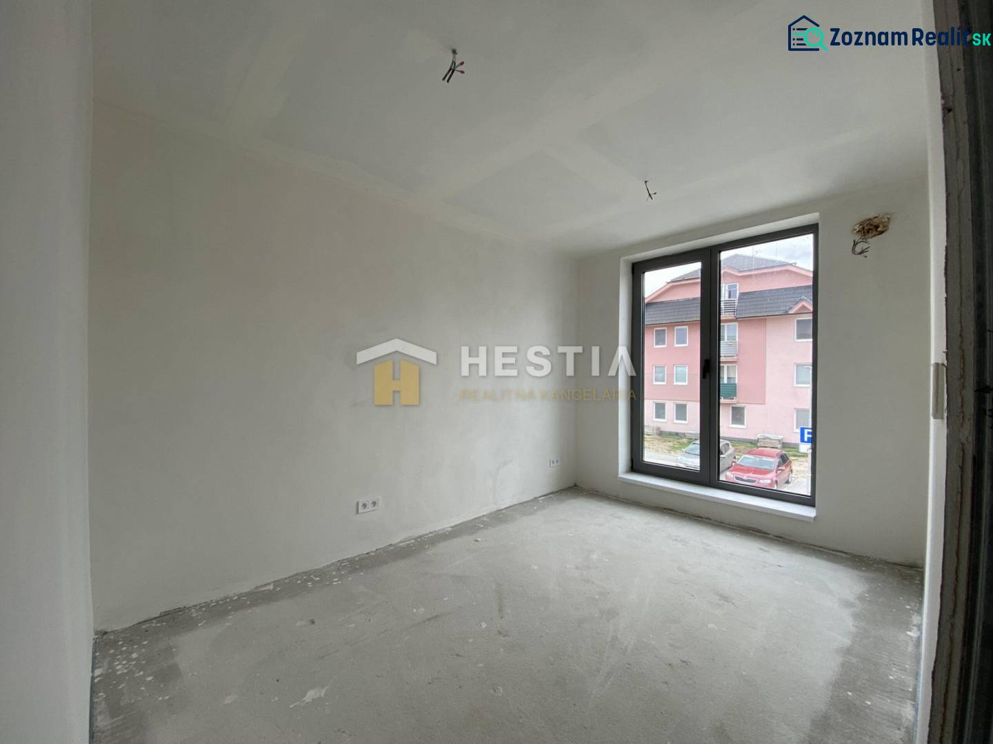 Ein Zimmer in einer 2-Zimmer-Wohnung mit rohem Boden und einem großen Fenster mit Blick auf die Straße.