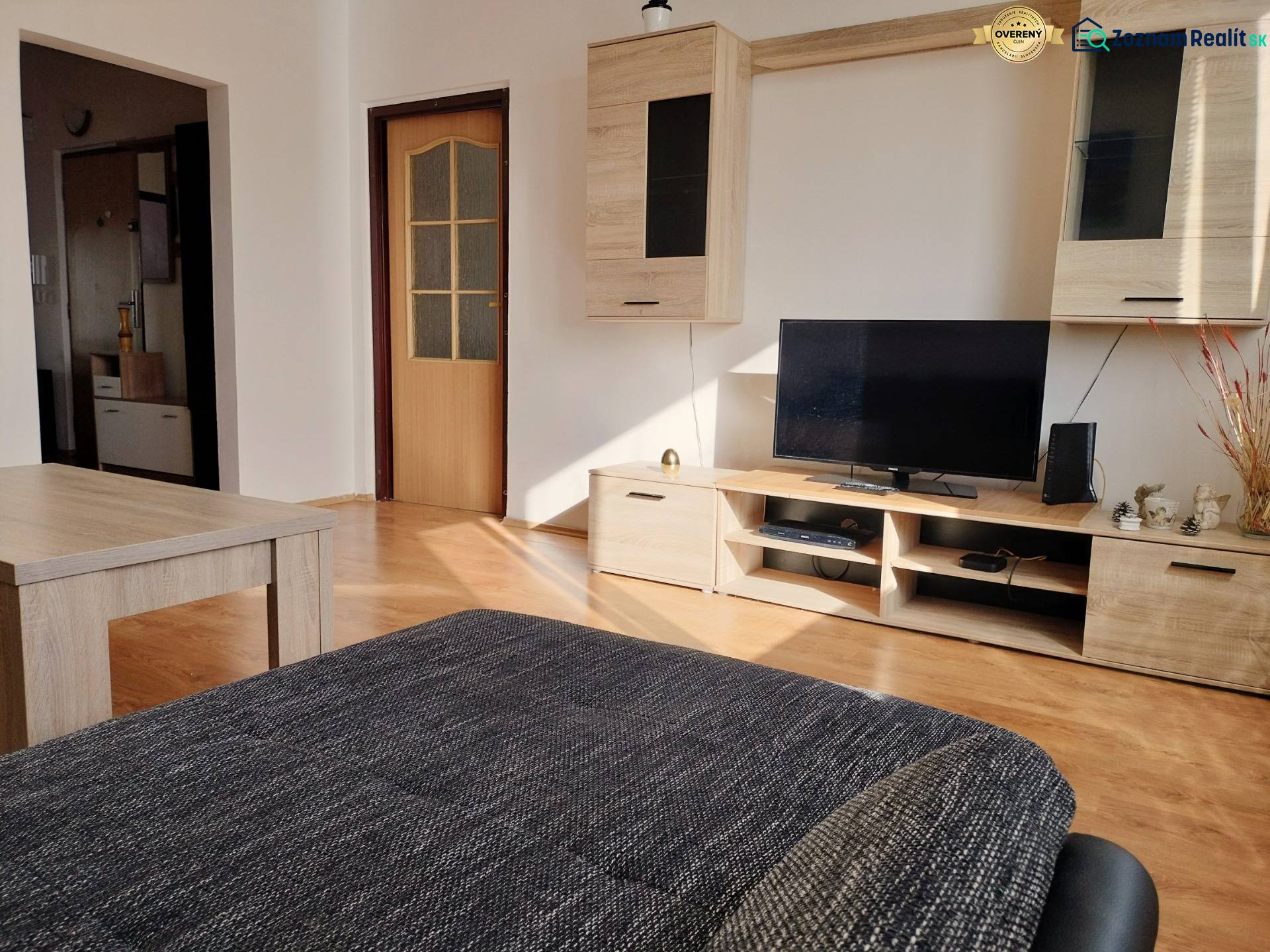 Wohnzimmer in einer 3-Zimmer-Wohnung mit Holzboden, Fernseher und Möbeln.