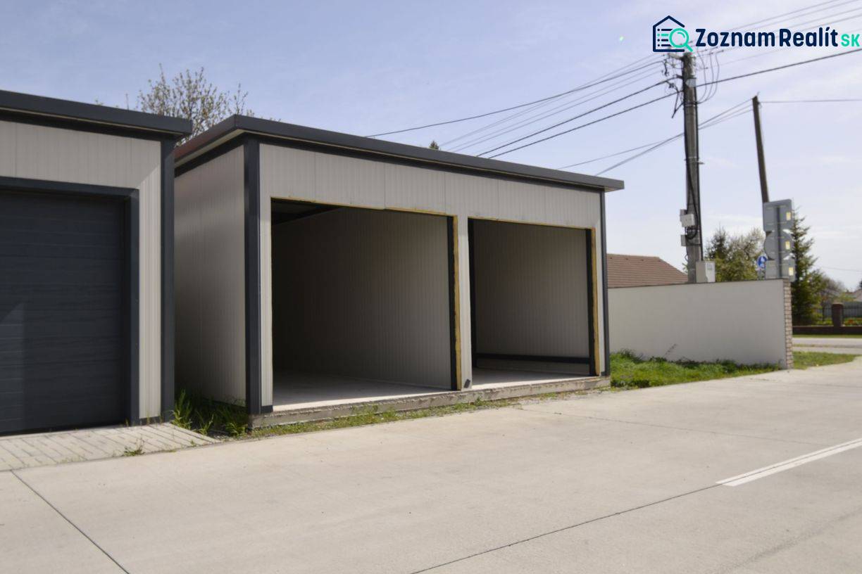 Garagen in Michal na Ostrove mit zwei offenen Einfahrten, neben der Straße und dem Zaun.