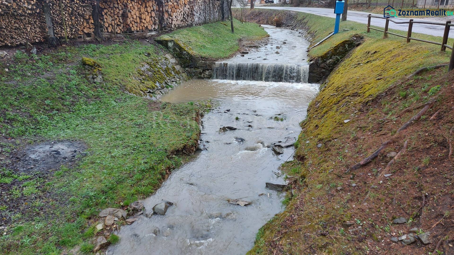 Ein Bach, der durch die Erholungsgebiete in Púchov fließt, mit Holz, das am Rand gelagert ist.