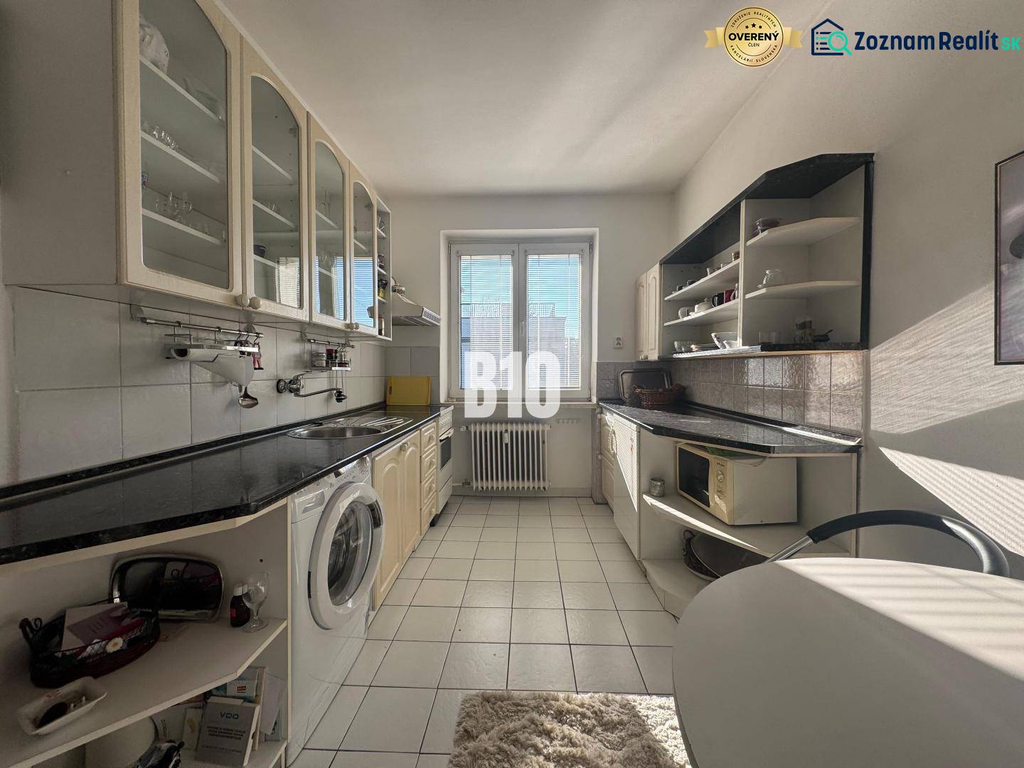 Küche in einer 2-Zimmer-Wohnung mit weißen Schränken und schwarzer Arbeitsplatte.