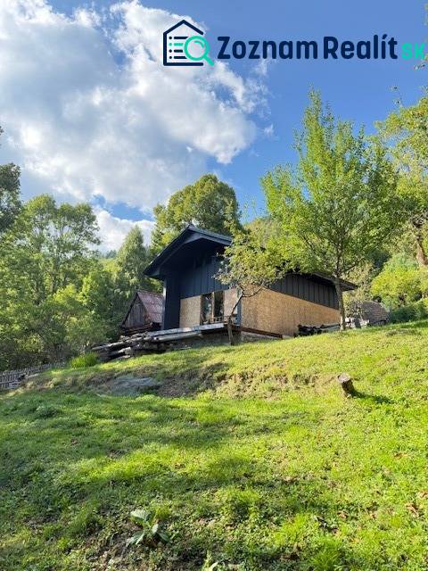 Eine Hütte in Horna Marikova, umgeben von grünen Bäumen an einem sonnigen Hang unter blauem Himmel.