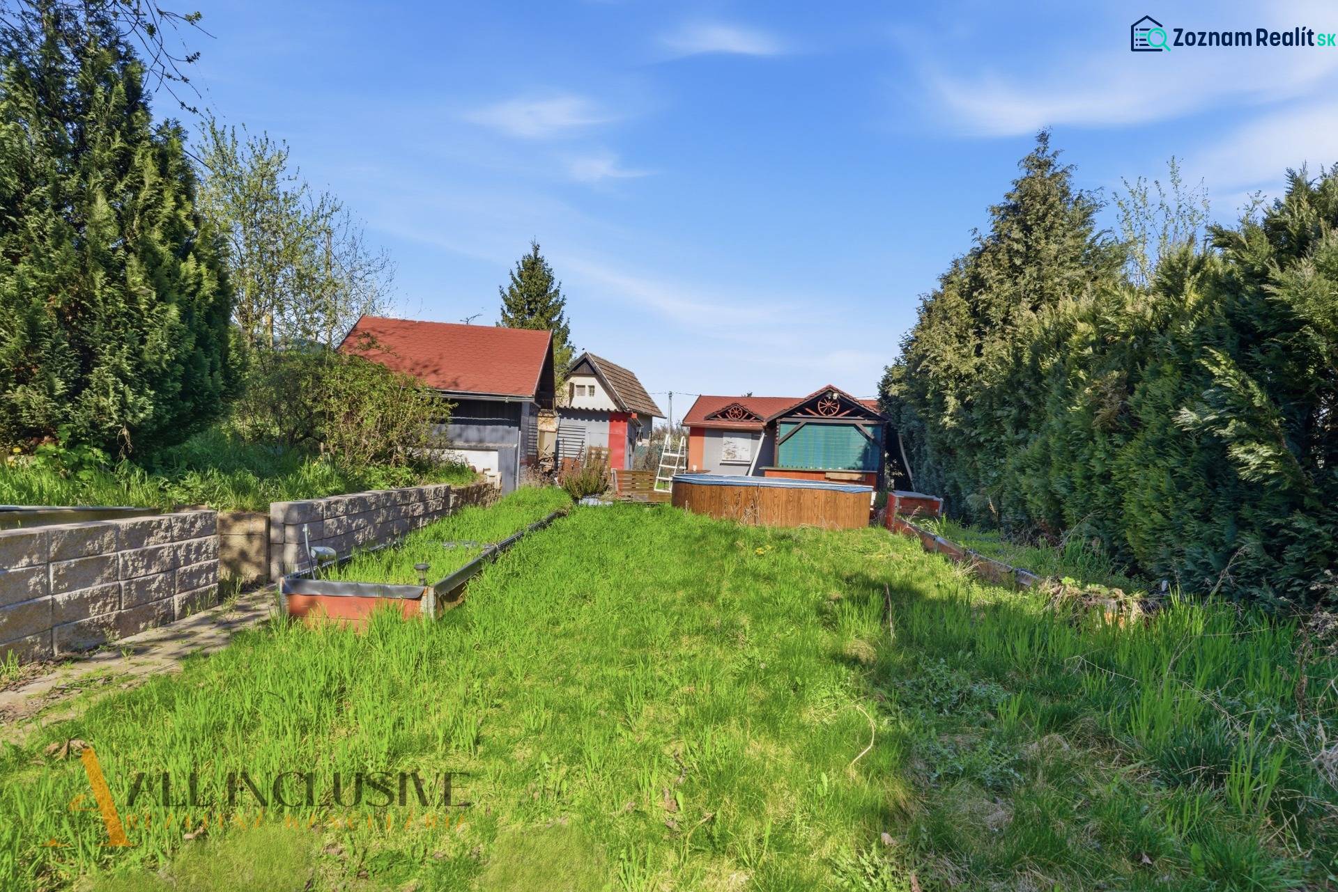 Gärten in Kráľová nad Váhom mit einem Häuschen, dichter Vegetation und Rasen unter blauem Himmel.