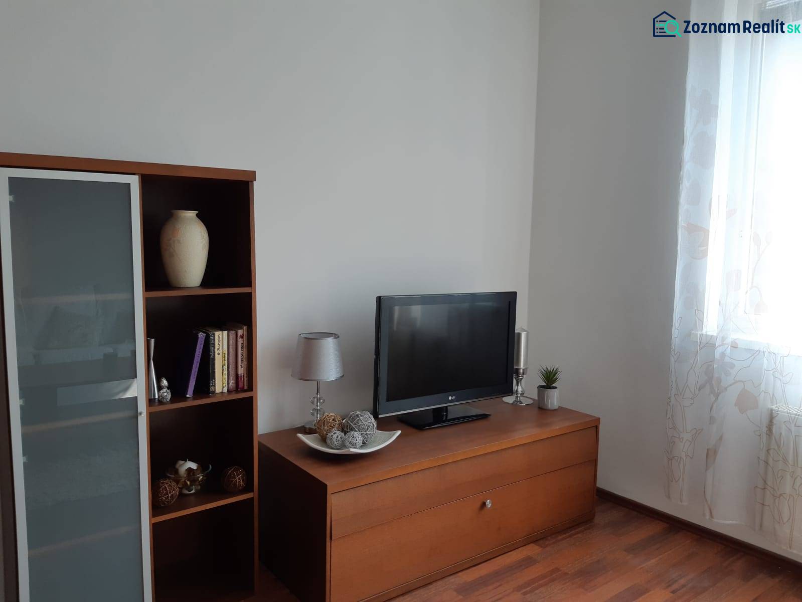 Wohnzimmer mit Holzboden, Bücherregal, Fernseher und dekorativen Gegenständen.