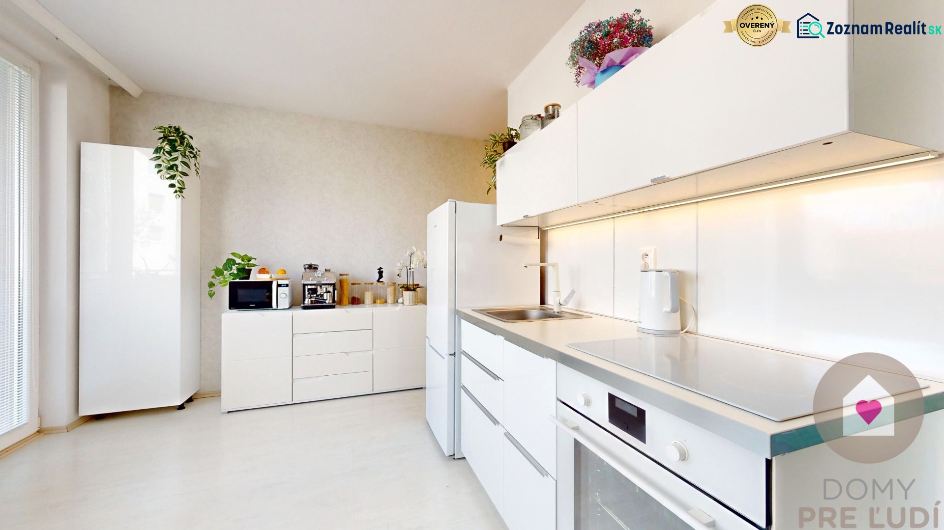 Küche in einer Einzimmerwohnung mit weißer Küchenzeile und Geräten, Boden mit Holzdekor.