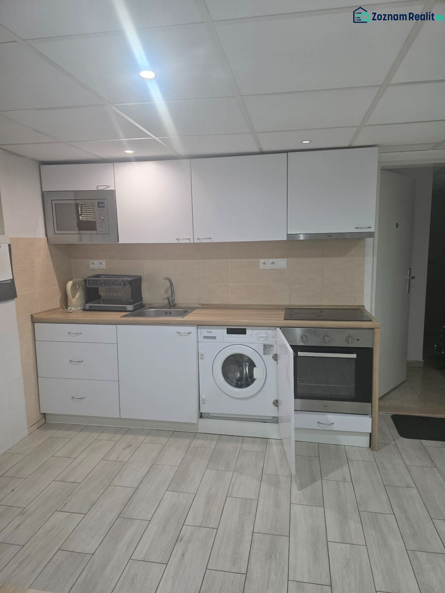 Küche in einer Einzimmerwohnung mit weißer Küchenzeile und Boden in Holzoptik.