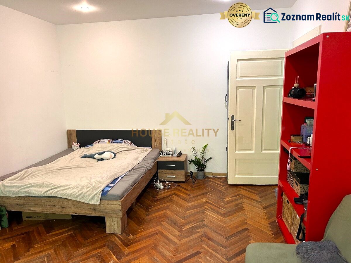 Schlafzimmer mit Bett, rotem Regal und Holzboden in einer Zweizimmerwohnung.