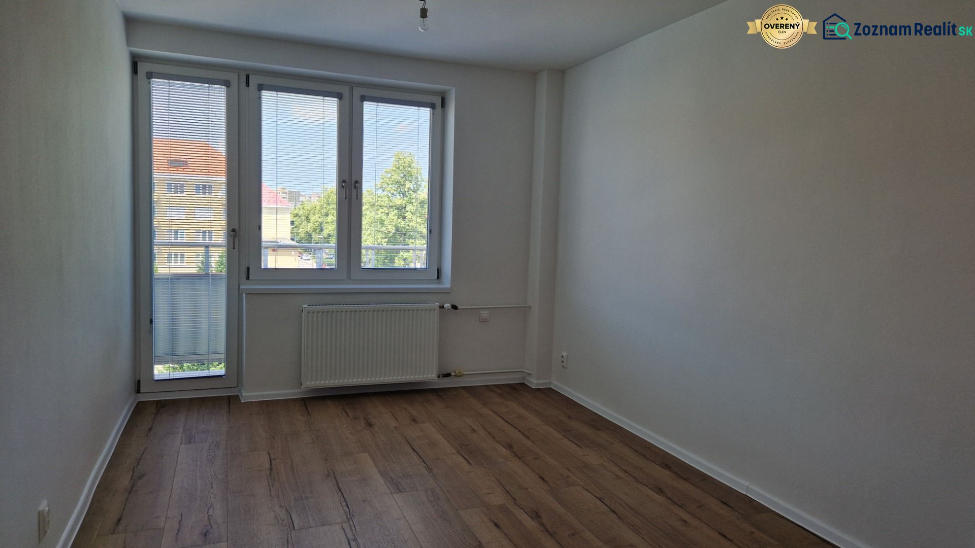 Ein Zimmer in einer 3-Zimmer-Wohnung mit einem Holzboden, einem großen Fenster und einem Heizkörper.