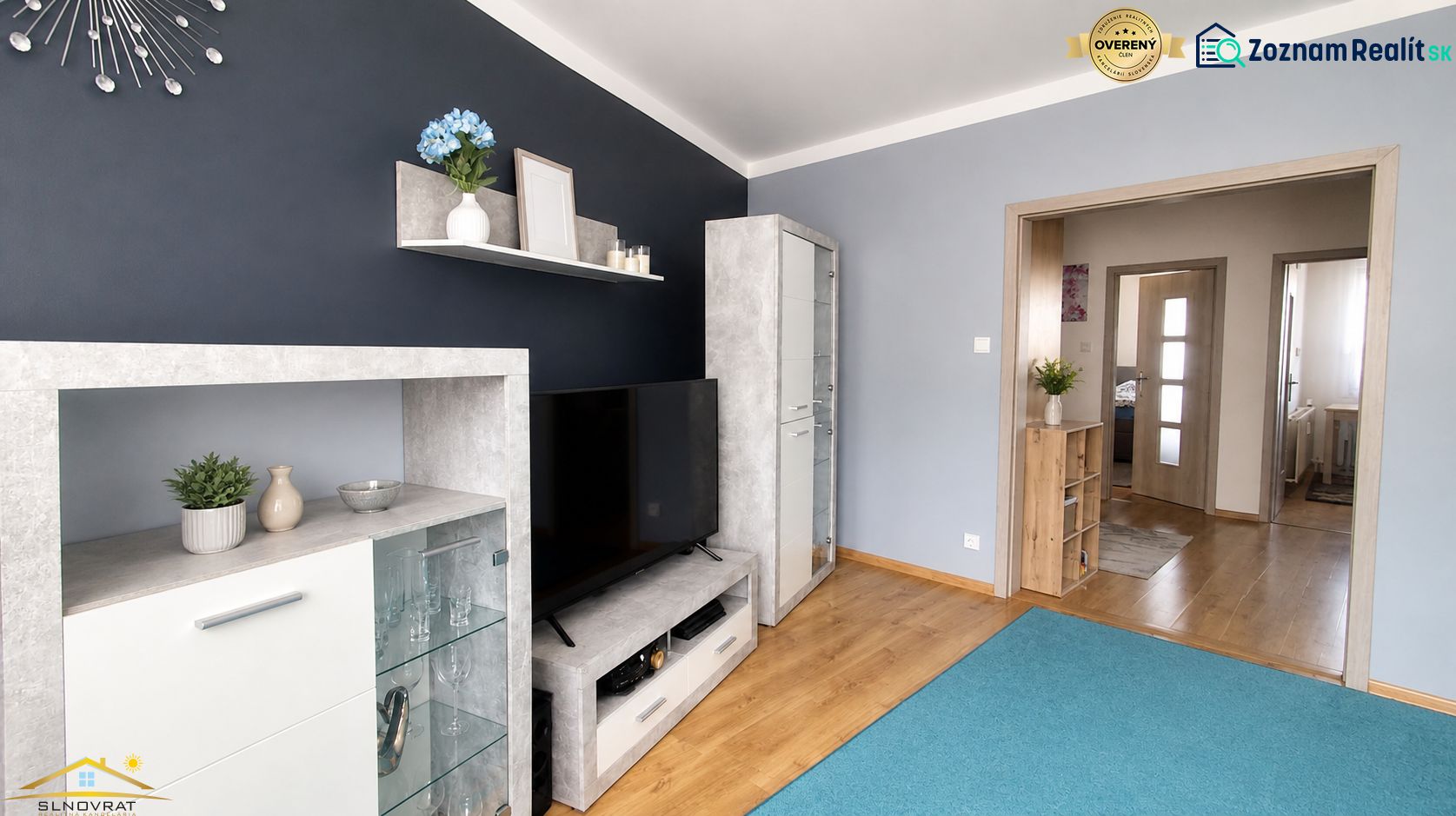 Wohnzimmer in einer 3-Zimmer-Wohnung mit Regalen, Fernseher und Holzboden.