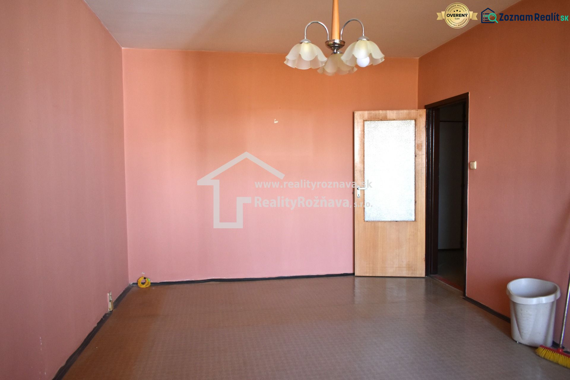Ein Zimmer mit rosa Wänden und braunem Boden in einer 3-Zimmer-Wohnung.