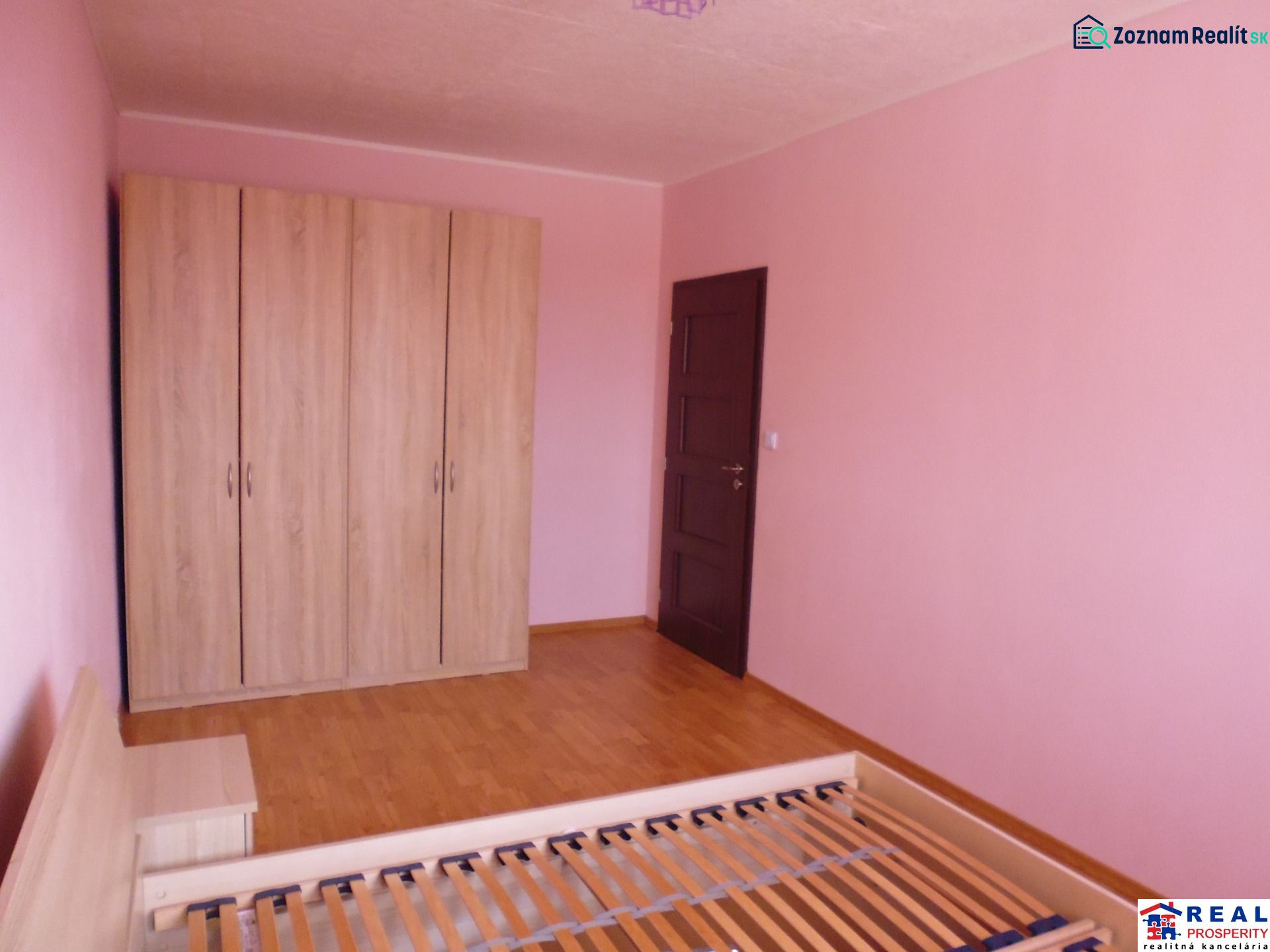 Ein Zimmer in einer 2-Zimmer-Wohnung mit rosa Wänden, einem Schrank und einem Boden in Holzoptik.