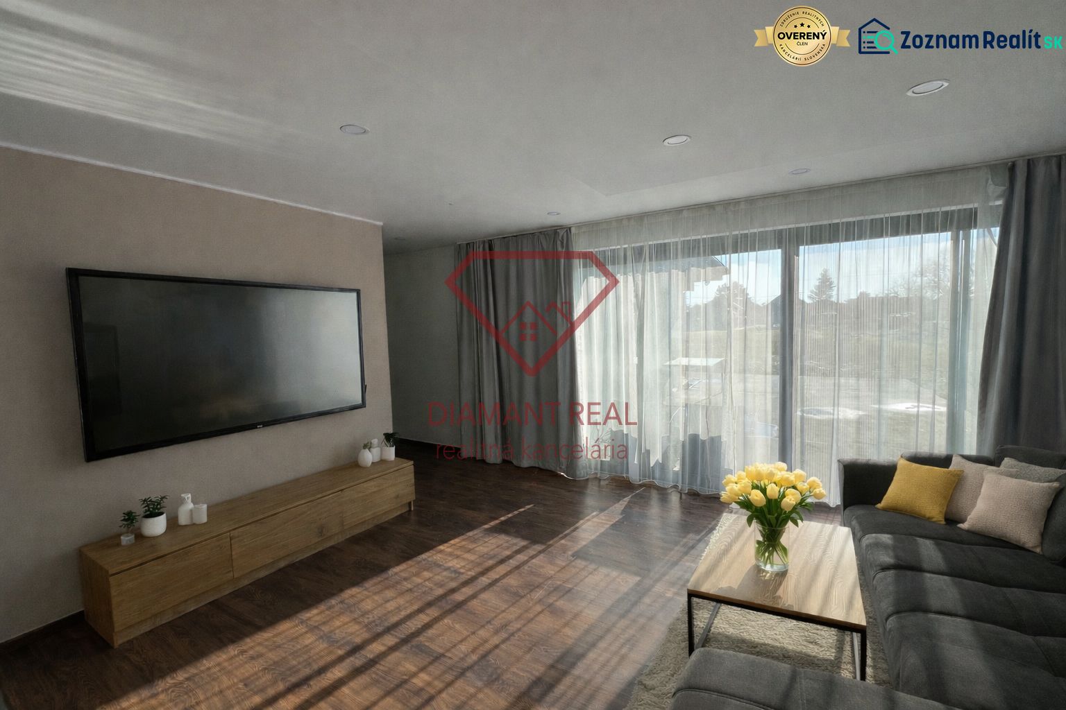 Wohnzimmer in einem Einfamilienhaus mit großem Fernseher, Sofa und Holzboden.