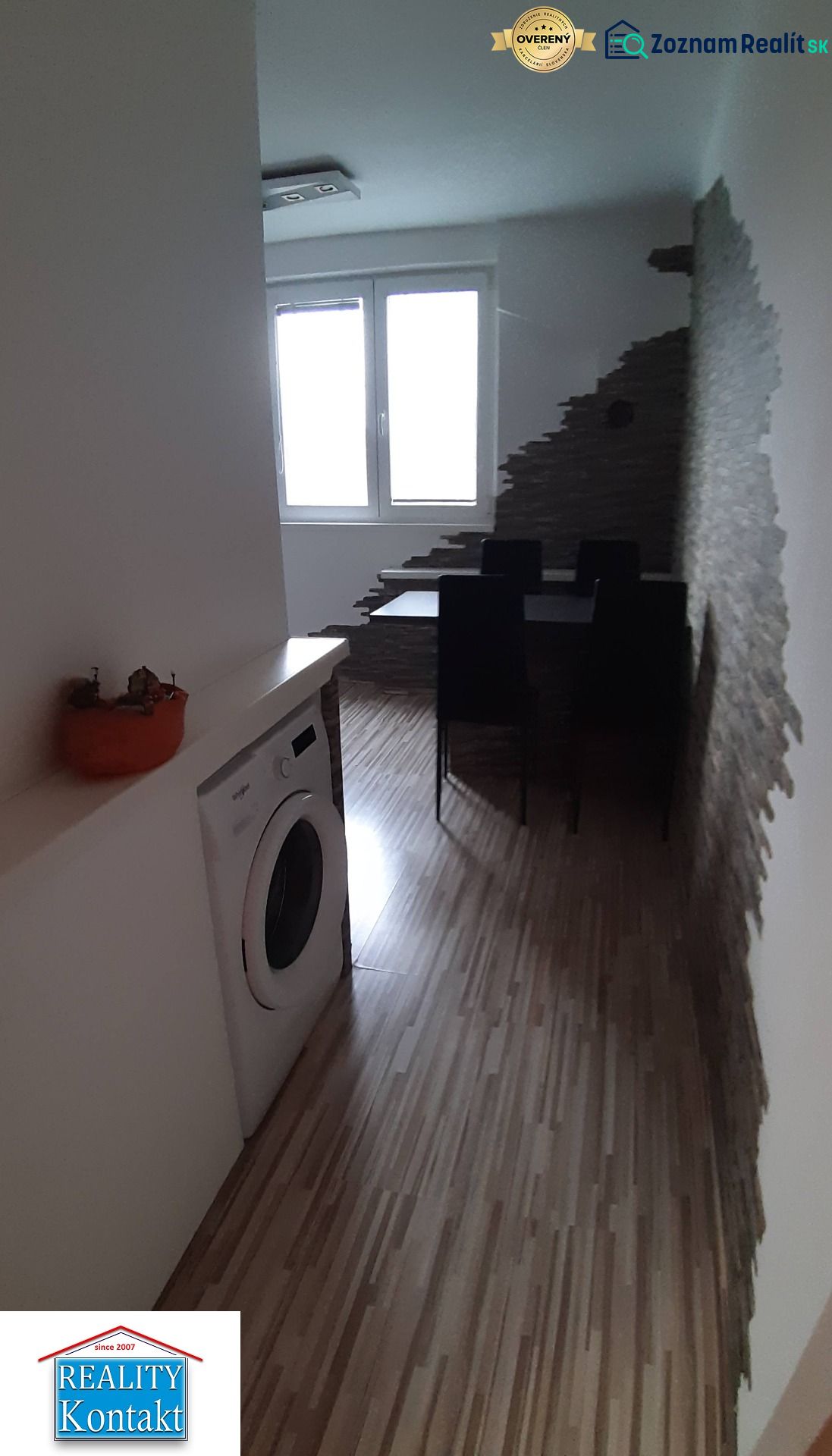 Essbereich mit Holzboden, Waschmaschine und interessanter Wand in einer 2-Zimmer-Wohnung.