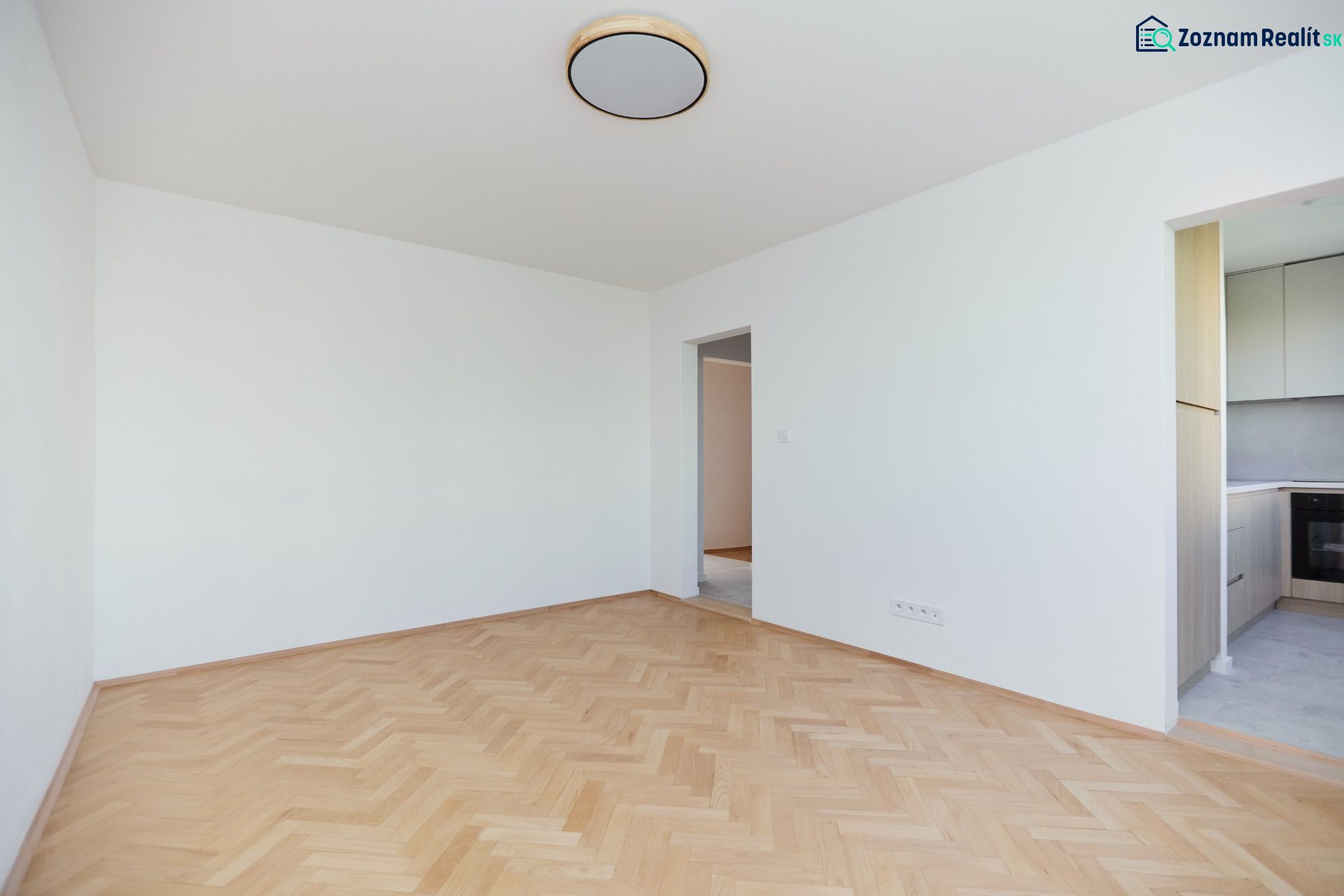 Ein leerer Raum mit Holzboden-Dekor und Blick in die Küche in einer 3-Zimmer-Wohnung.