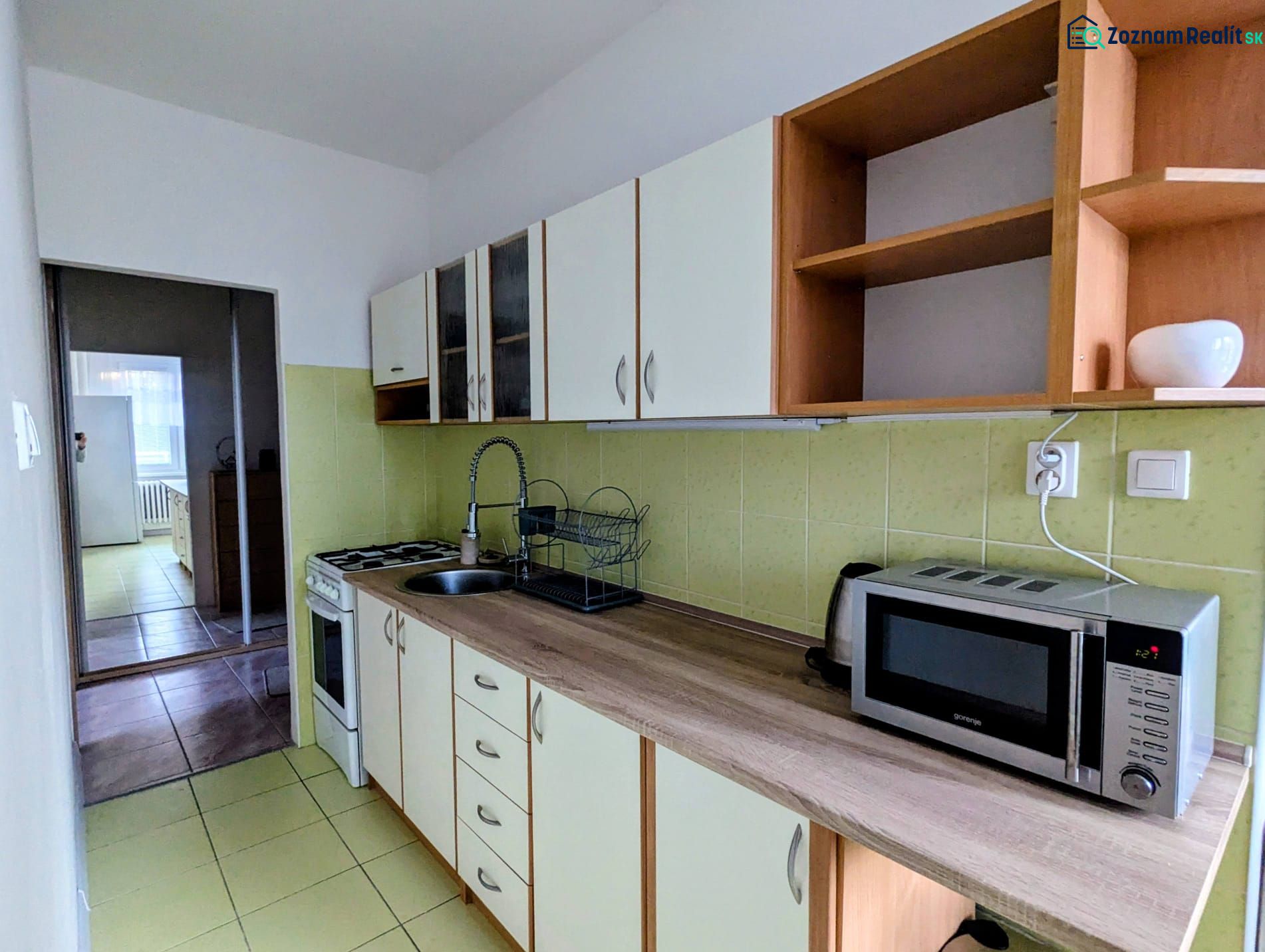 Küche in einer 2-Zimmer-Wohnung mit Mikrowelle und Kochfeld, die in einen weiteren Raum führt.