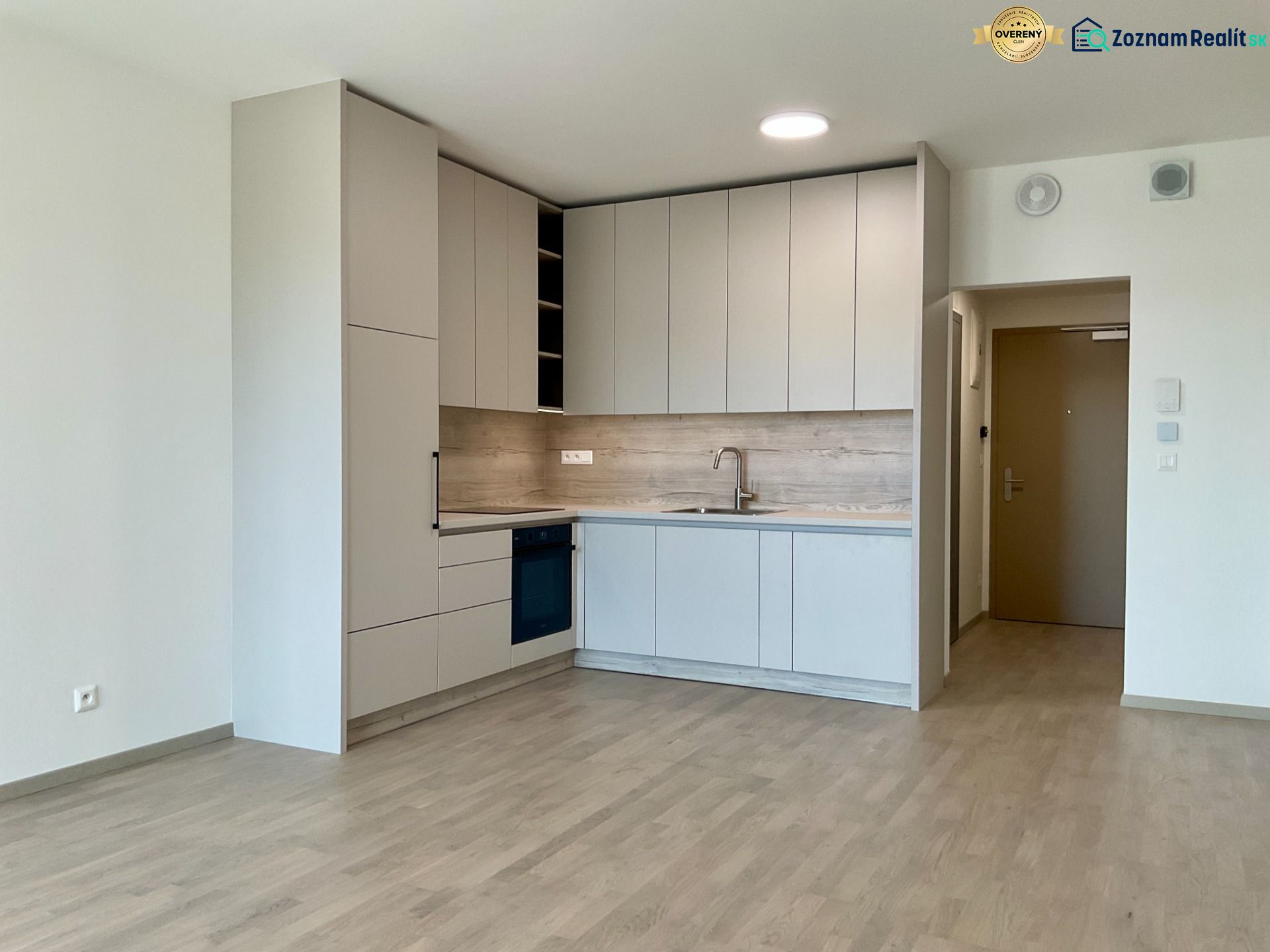 Moderne Küche in einer Einzimmerwohnung, helle Schränke, Boden mit Holzdekor, neutraler Stil.
