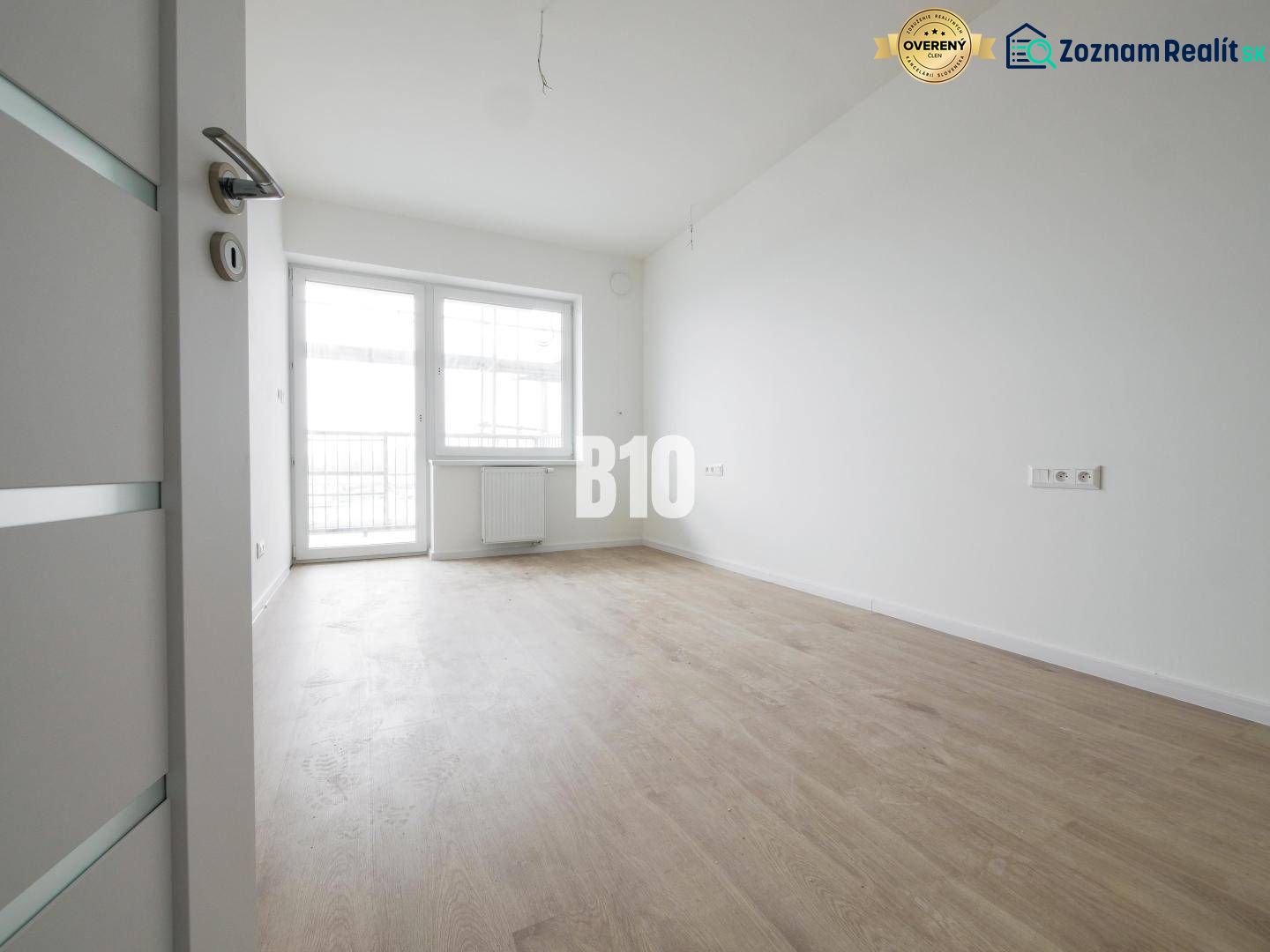 Ein geräumiges Zimmer mit einem großen Fenster, hellem Boden und weißen Wänden in einer 2-Zimmer-Wohnung.