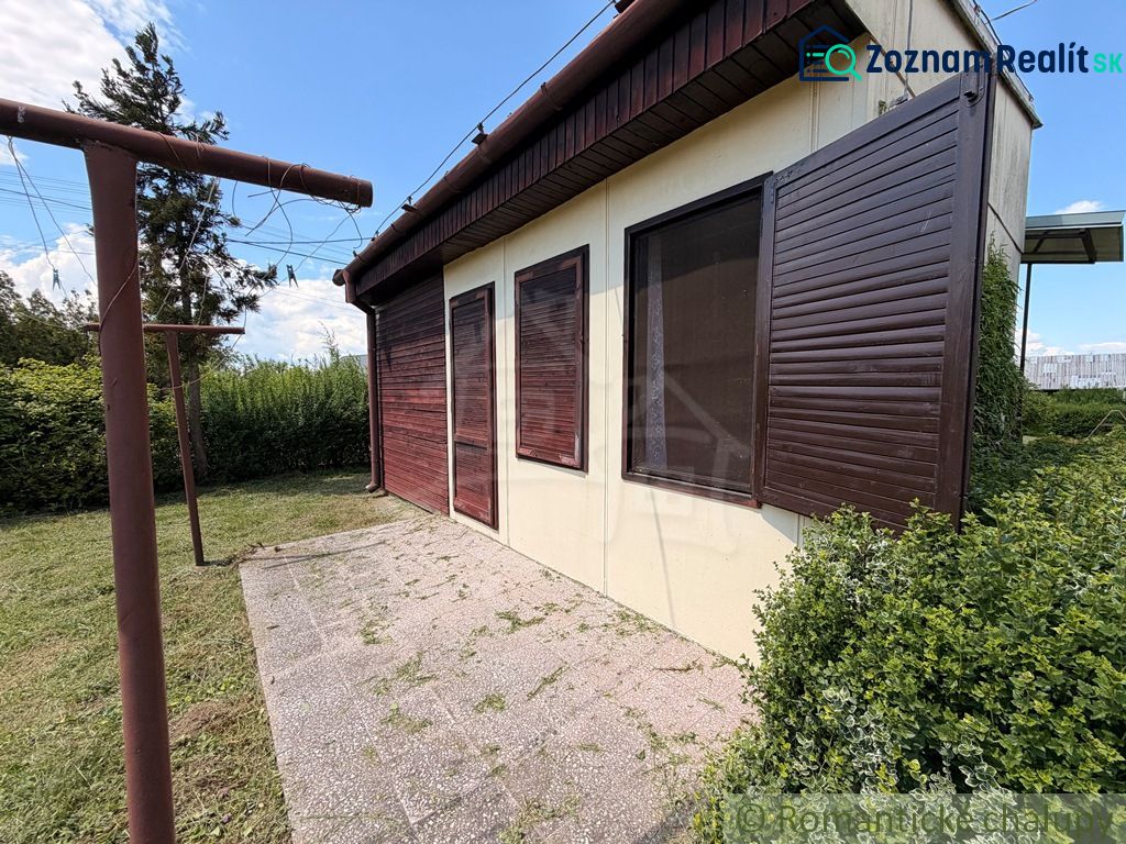 Eine Hütte in Nové Zámky mit geschlossenen hölzernen Fensterläden und umgebendem Grün im Garten.