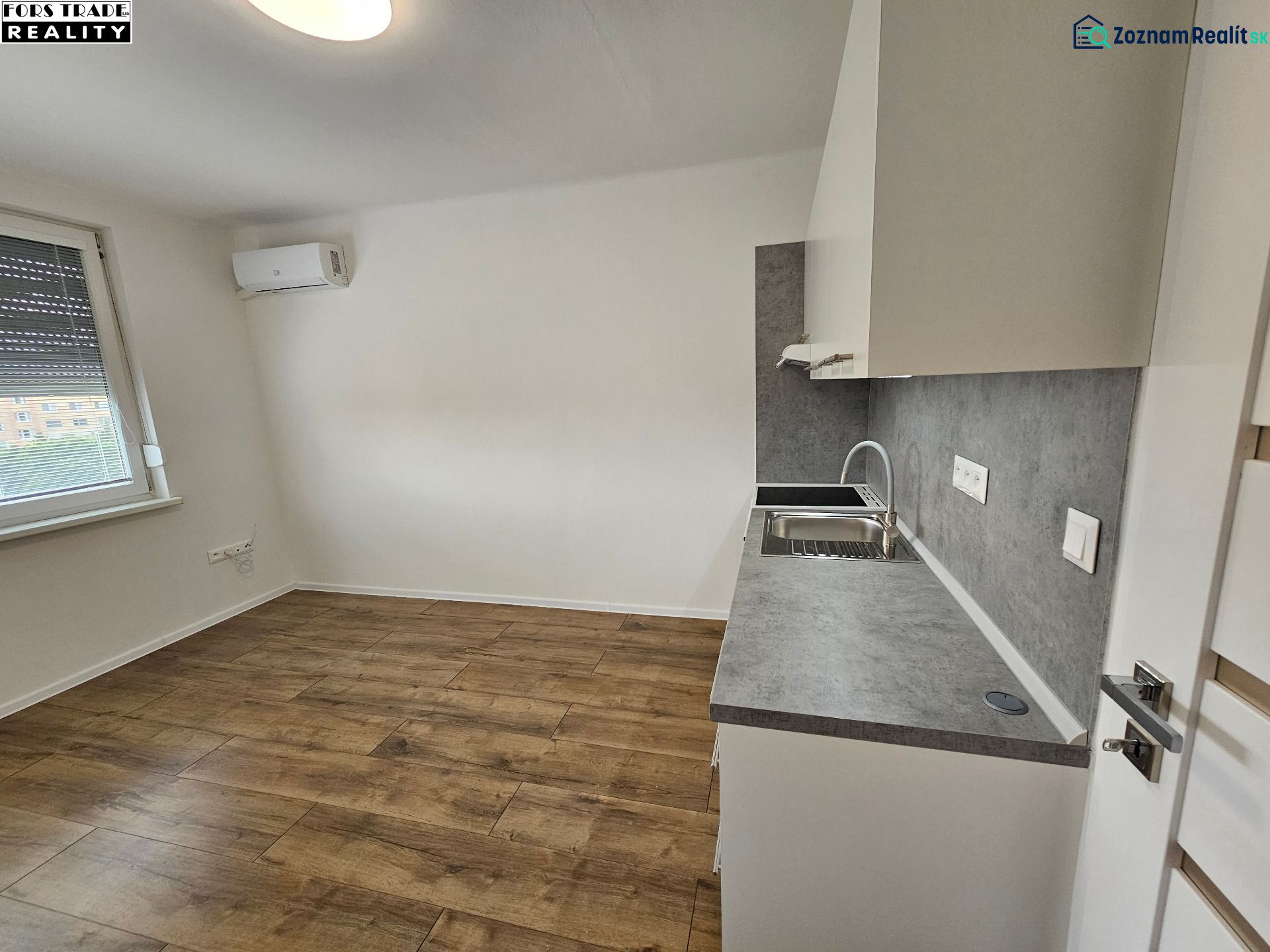 Einzimmerwohnung mit Küchenzeile und Boden in Holzoptik, Klimaanlage und Fenster.
