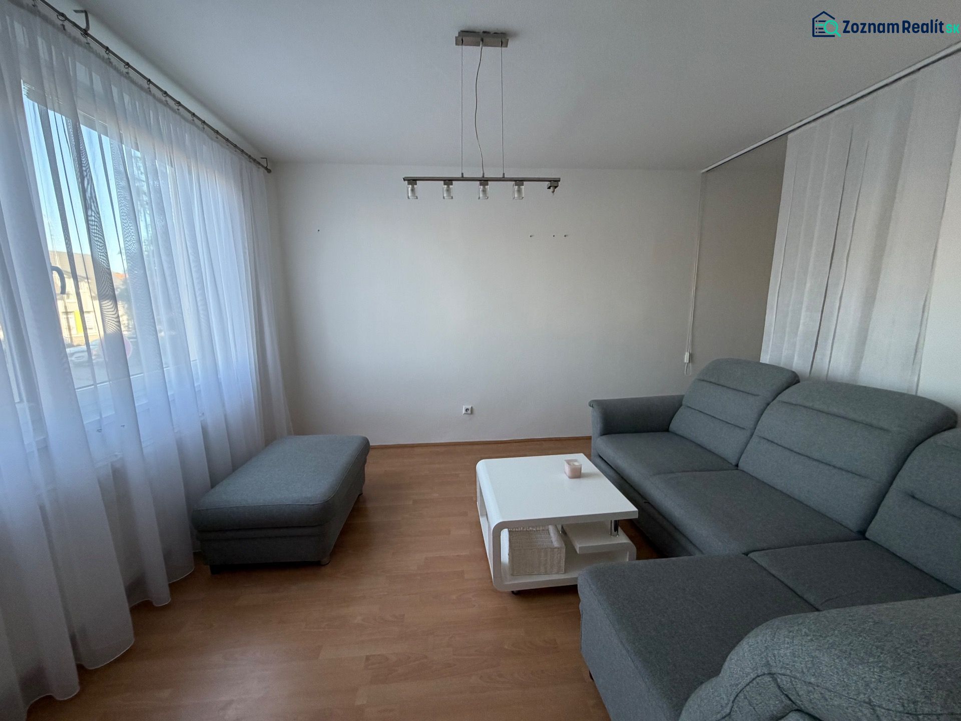 Wohnzimmer mit grauem Sofa, Couchtisch und Boden in Holzoptik in einer 3-Zimmer-Wohnung.