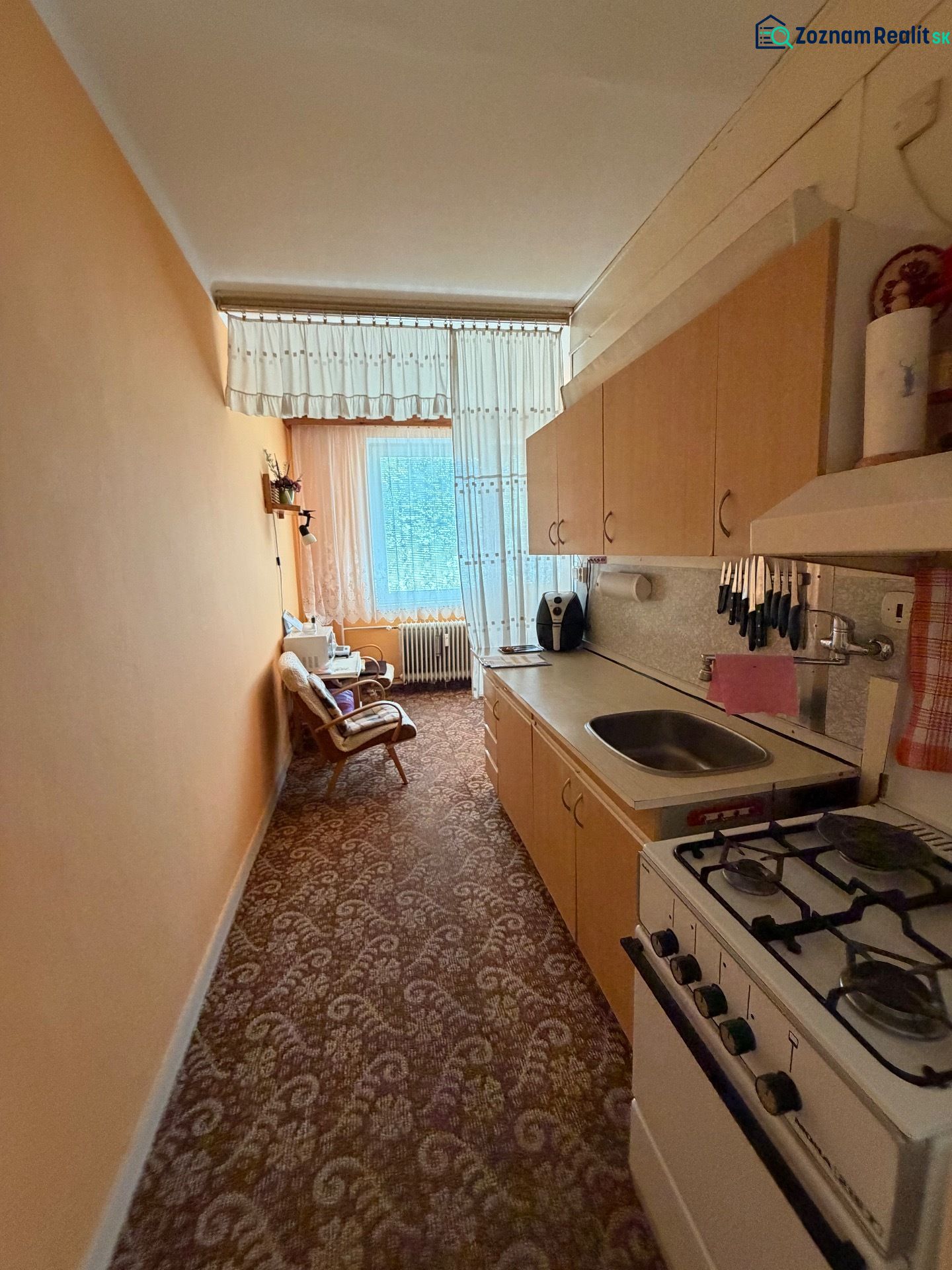 Schmale Küche in einer 2-Zimmer-Wohnung mit einem Gasherd und einem Blumenmuster auf dem Teppich.