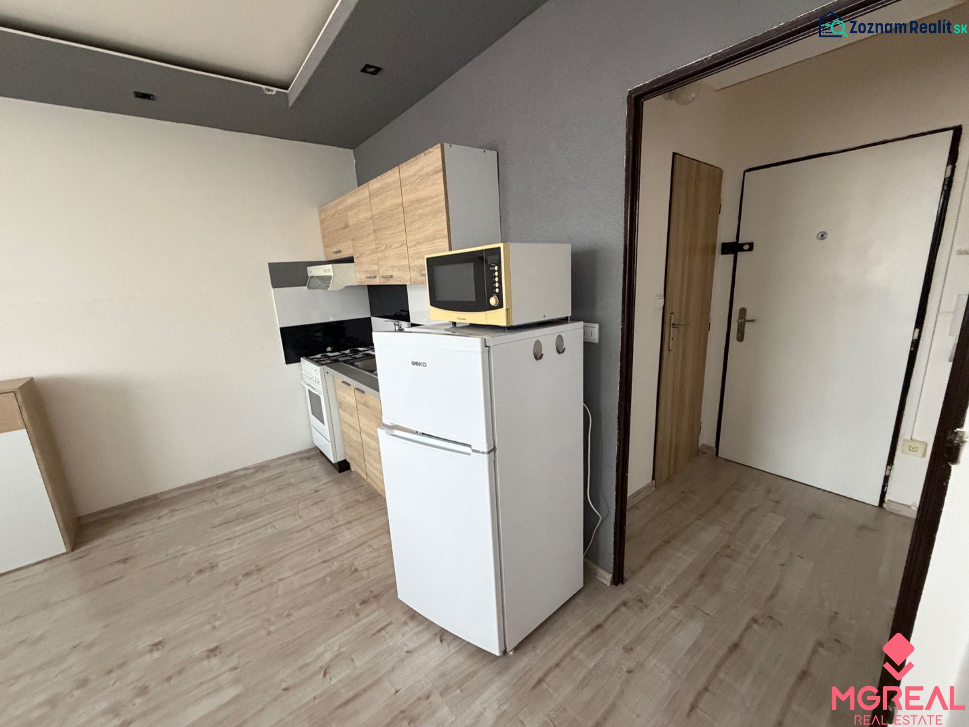 Küche in einer Einzimmerwohnung mit Kühlschrank und Boden in Holzoptik.