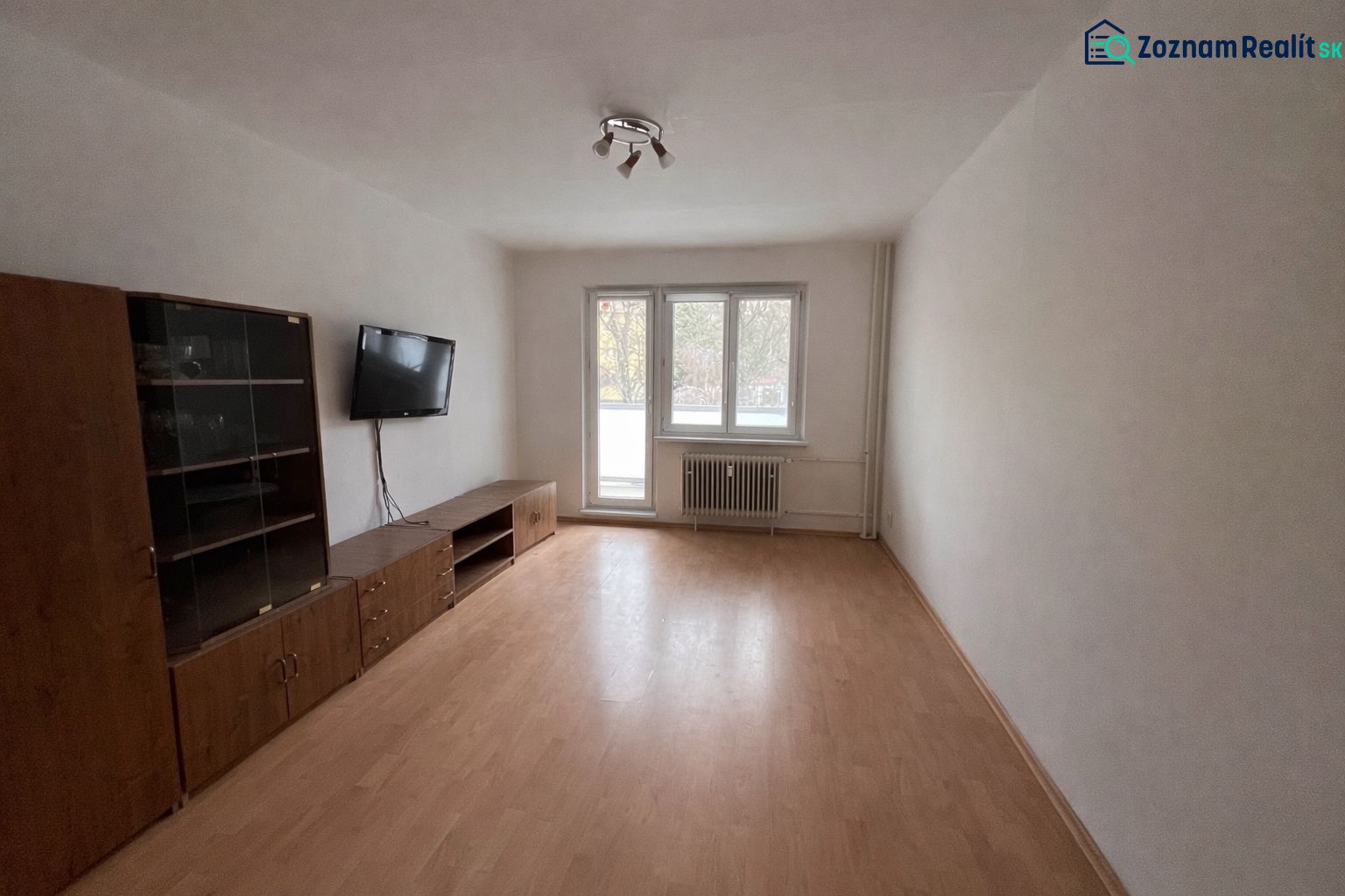 Wohnzimmer in einer Zweizimmerwohnung mit Holzboden und einem an der Wand montierten Fernseher.