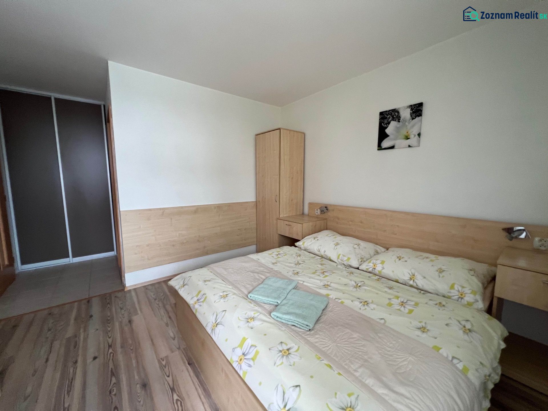 Schlafzimmer in einer 2-Zimmer-Wohnung mit Holzboden, hellen Möbeln und einem Bild an der Wand.
