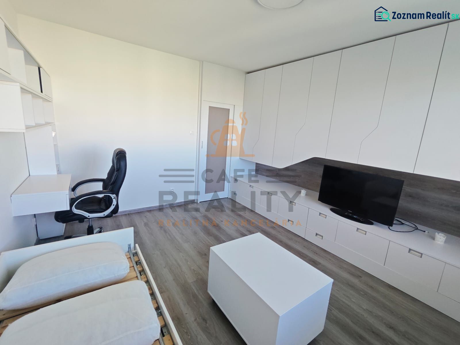 Innenraum einer Einzimmerwohnung mit Schreibtisch, Fernseher und Boden in Holzoptik.