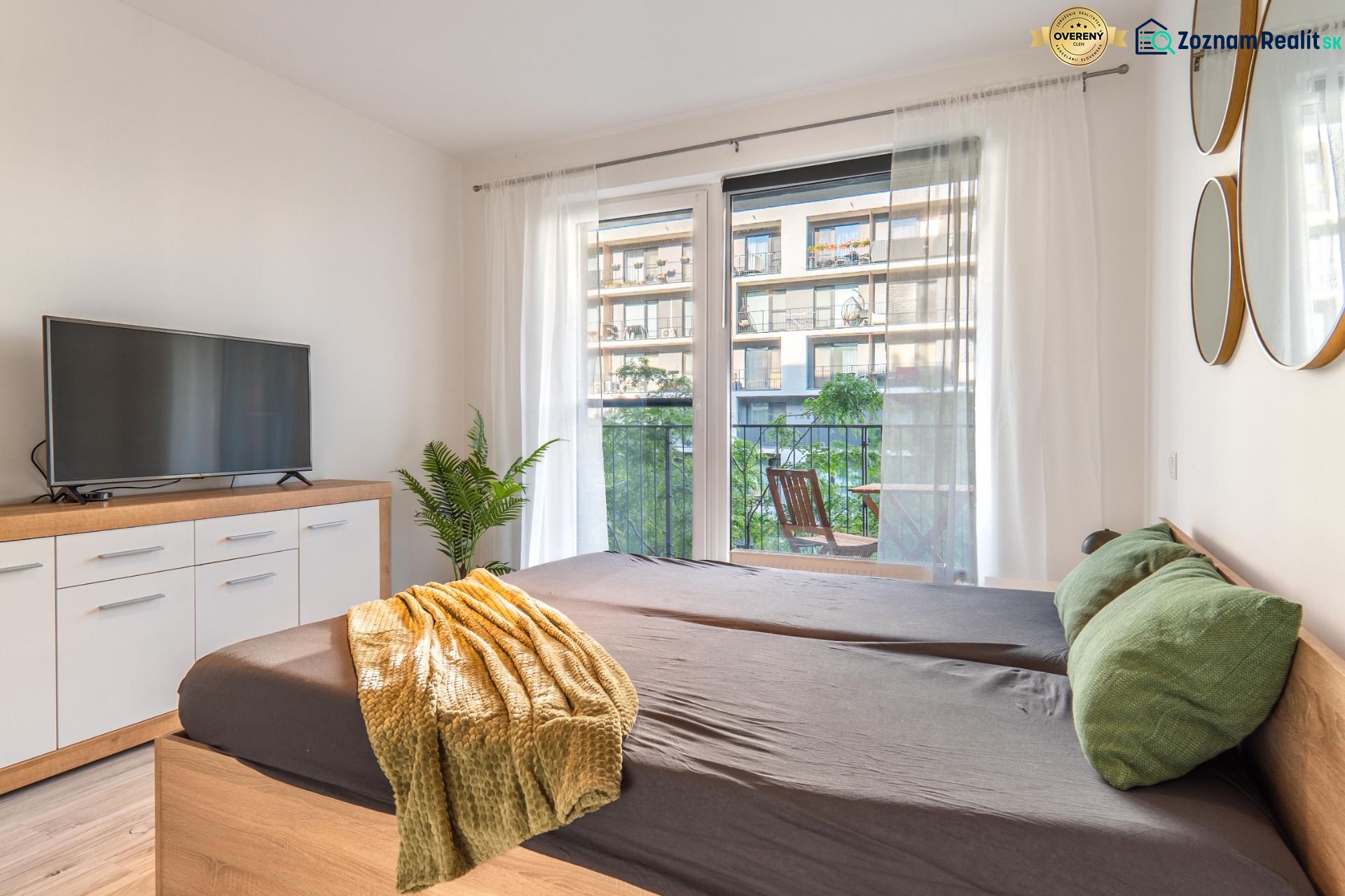 Schlafzimmer in einer Einzimmerwohnung mit Fernseher, Spiegeln und Balkon, Boden mit Holzdekor.