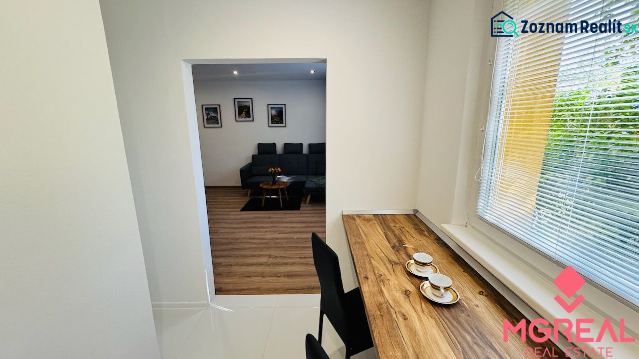 Innenraum einer Einzimmerwohnung mit Holzboden, Sofa und Tisch am Fenster.