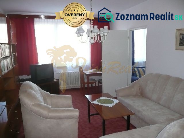 Wohnzimmer in einer Zweizimmerwohnung mit rotem Teppich und beigem Sofa.