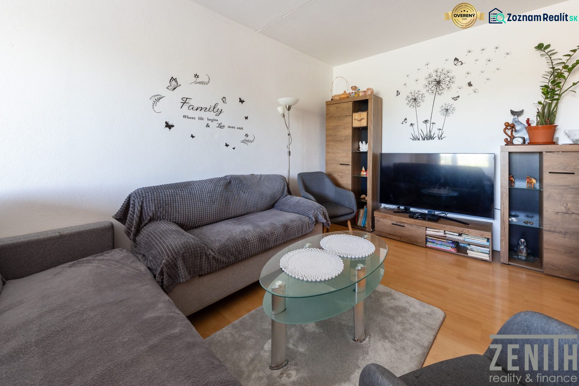 Wohnzimmer mit Holzboden, Sofa, Glastisch und Fernseher.