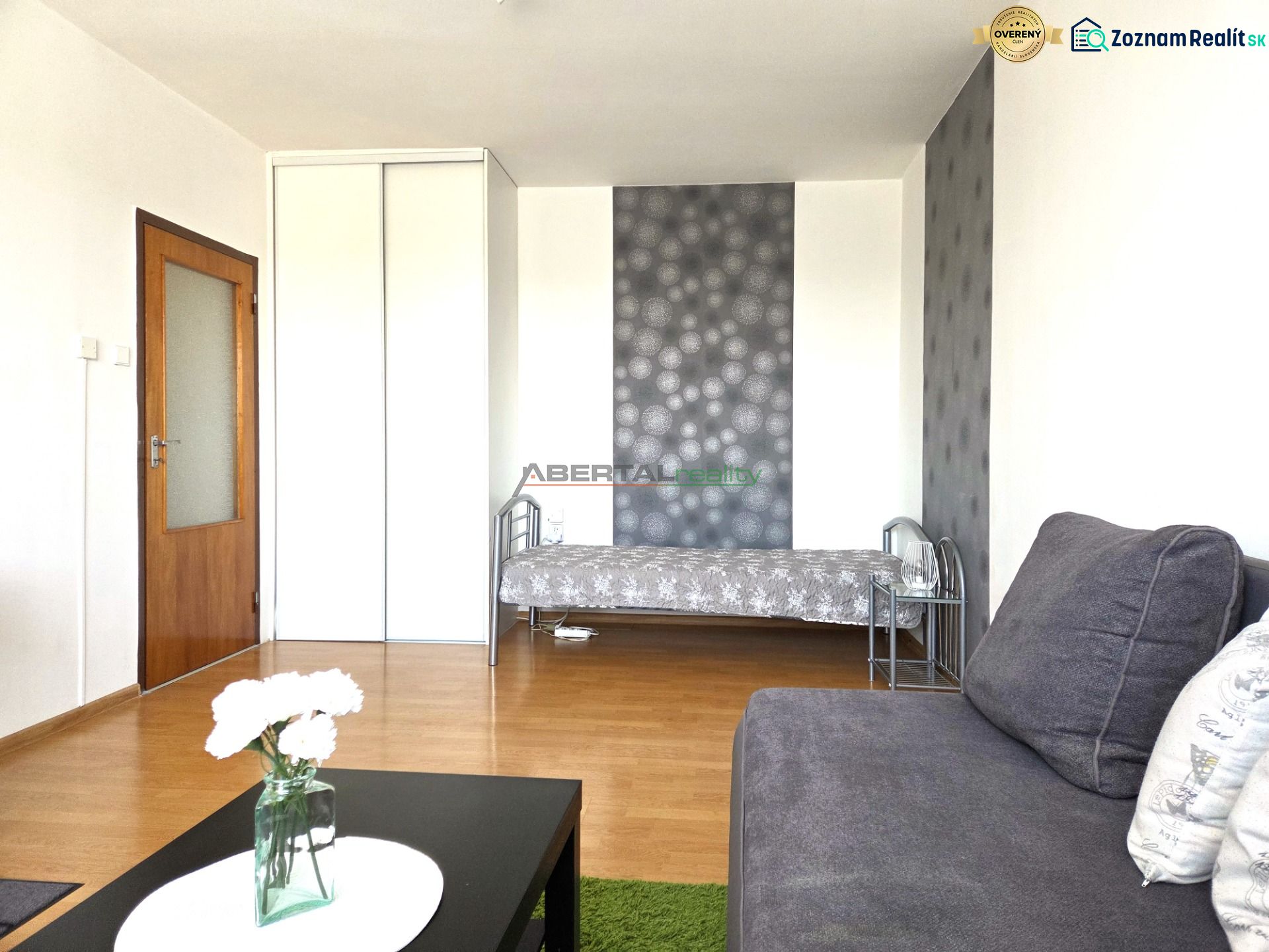 Wohnzimmer einer Einzimmerwohnung mit Sofa, Bett und Boden in Holzoptik.