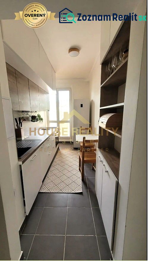 Eine schmale Küche in einer 3-Zimmer-Wohnung mit weißen Schränken und dunklem Boden.