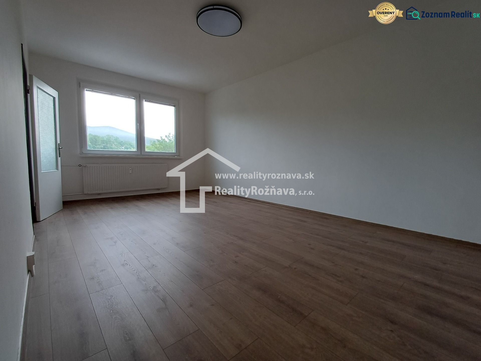Ein Zimmer in einer 3-Zimmer-Wohnung mit einem Boden in Holzoptik, einem großen Fenster und einem Heizkörper.