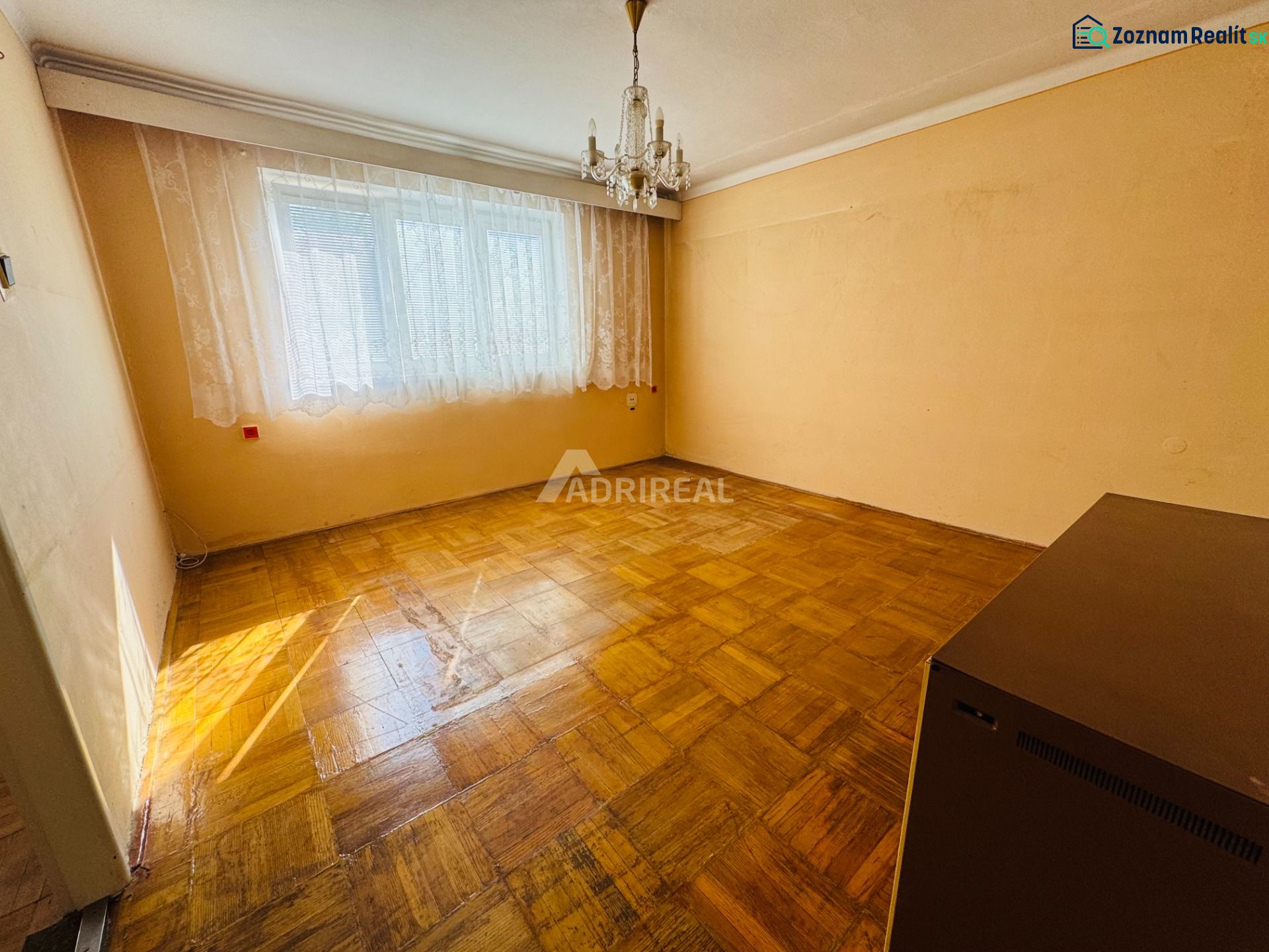 Ein Zimmer in einer 2-Zimmer-Wohnung mit einem Kristallleuchter und einem Boden in Holzoptik.