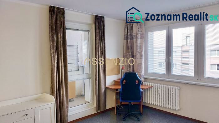 Einzimmerwohnung mit Fenstern, Vorhängen, Heizkörper und einem Tisch mit Stuhl.