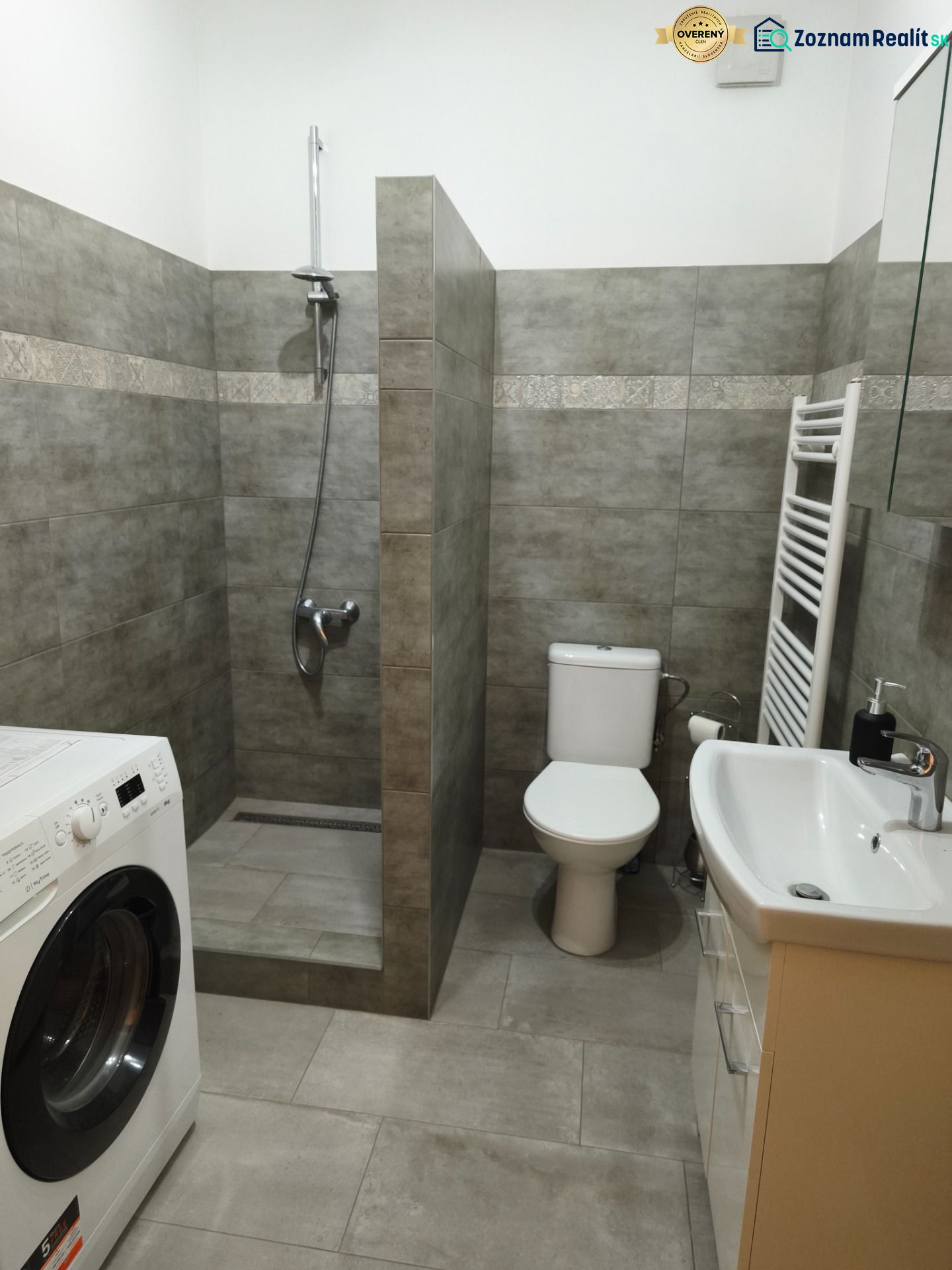 Kúpeľňa v 1-izbovom byte s práčkou, sprchovacím kútom a toaletou.

Badezimmer in einer Einzimmerwohnung mit Waschmaschine, Dusche und Toilette.